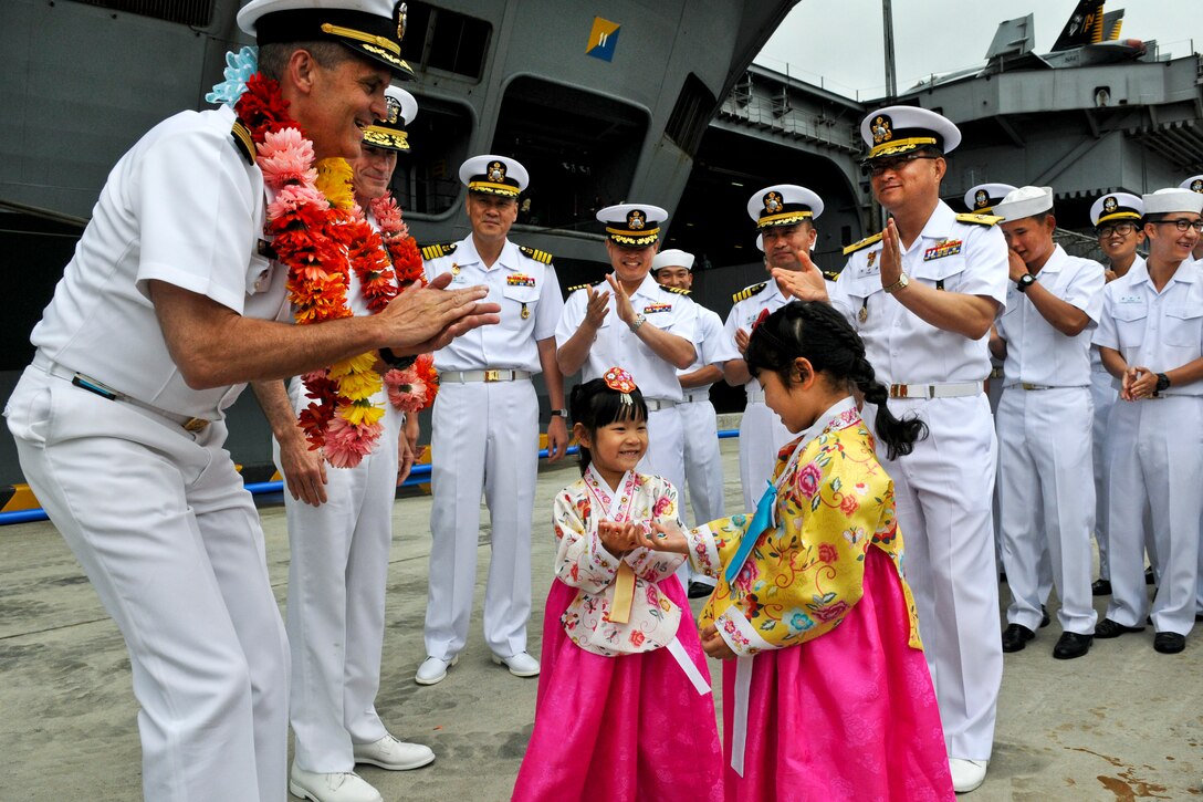 U.S. Navy Capt. David Lausman presents coins to children in traditional Korean dress at a welcome ceremony in Busan, Korea, June 27, 2012. Lausman is commanding officer of the aircraft carrier USS George Washington. Based in Japan, the the George Washington and its embarked air wing, Carrier Air Wing 5, arrived in Busan for a port visit.