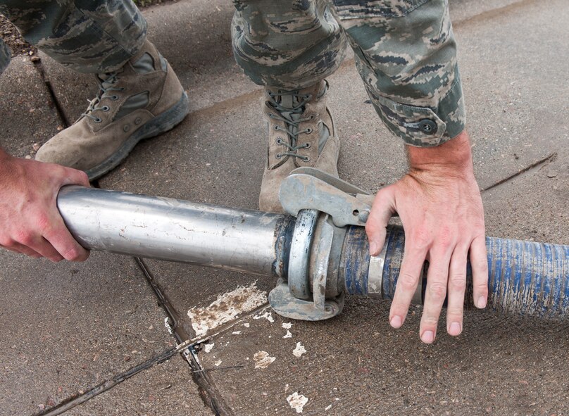 Senior Airman Joshua Peterson, 28th Civil Engineer Squadron water and fuels systems technician, attaches a nozzle to a hard wall hose during maintenance at Ellsworth Air Force Base, S.D., June 27, 2012. The hose is used to vacuum out debris such as leaves and garbage to prevent the sewer system from being clogged. (U.S. Air Force photo by Airman 1st Class Alystria Maurer/Released)