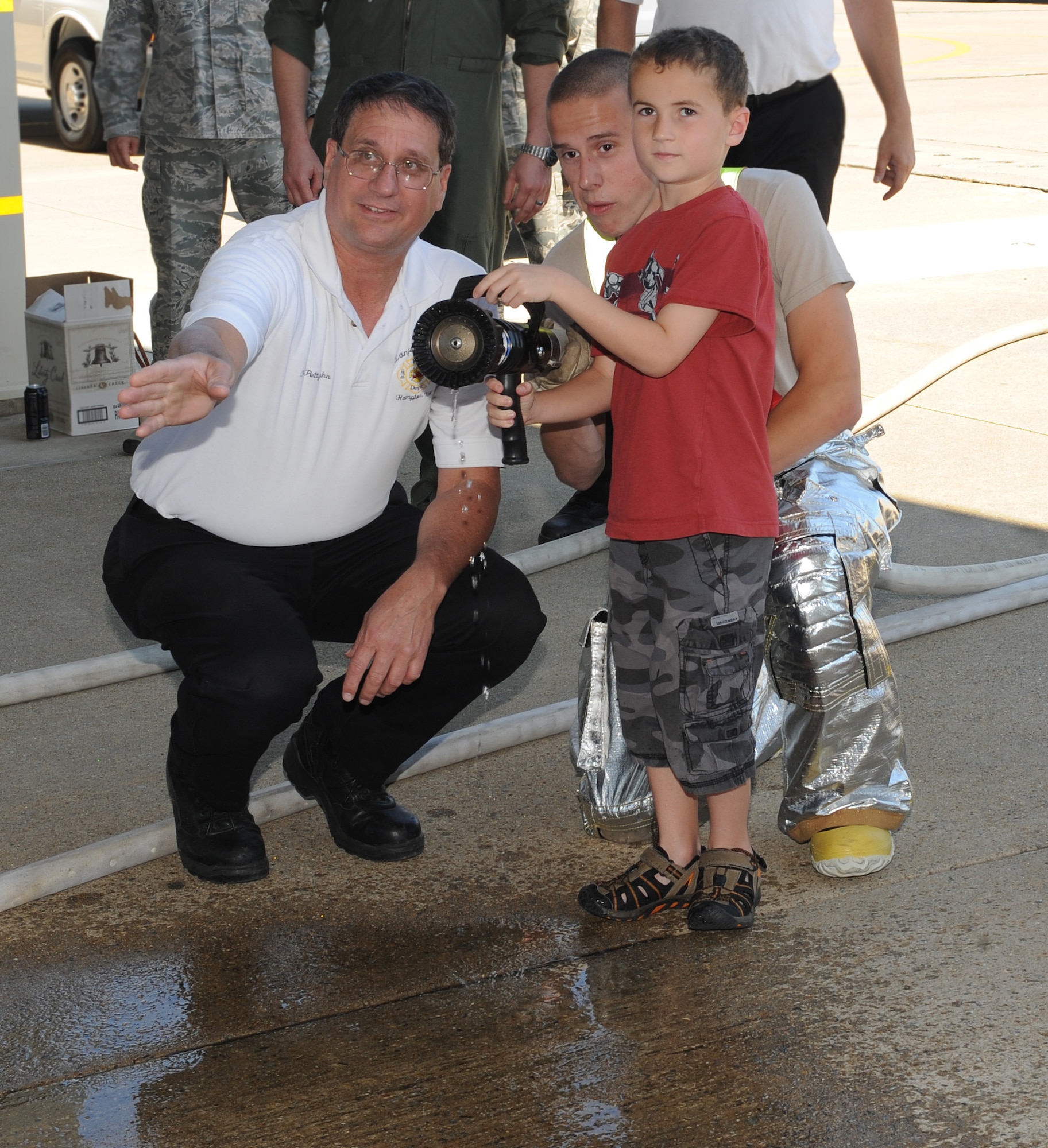 Rick Pettyjohn, 633rd Civil Engineer Squadron assistant chief of fire prevention, and Airman 1st Class Joshua Shelton, 633rd CES firefighter, show Wyatt, 8, how to soak his father, Lt. Col. Peter Fesler, 1st Operations Group deputy commander, with water after his final flight at Langley Air Force Base, Va., June 27, 2012. Fesler and his family will relocate to Washington, D.C., for his next assignment. (U.S. Air Force photo by Airman 1st Class Teresa Cleveland/Released)