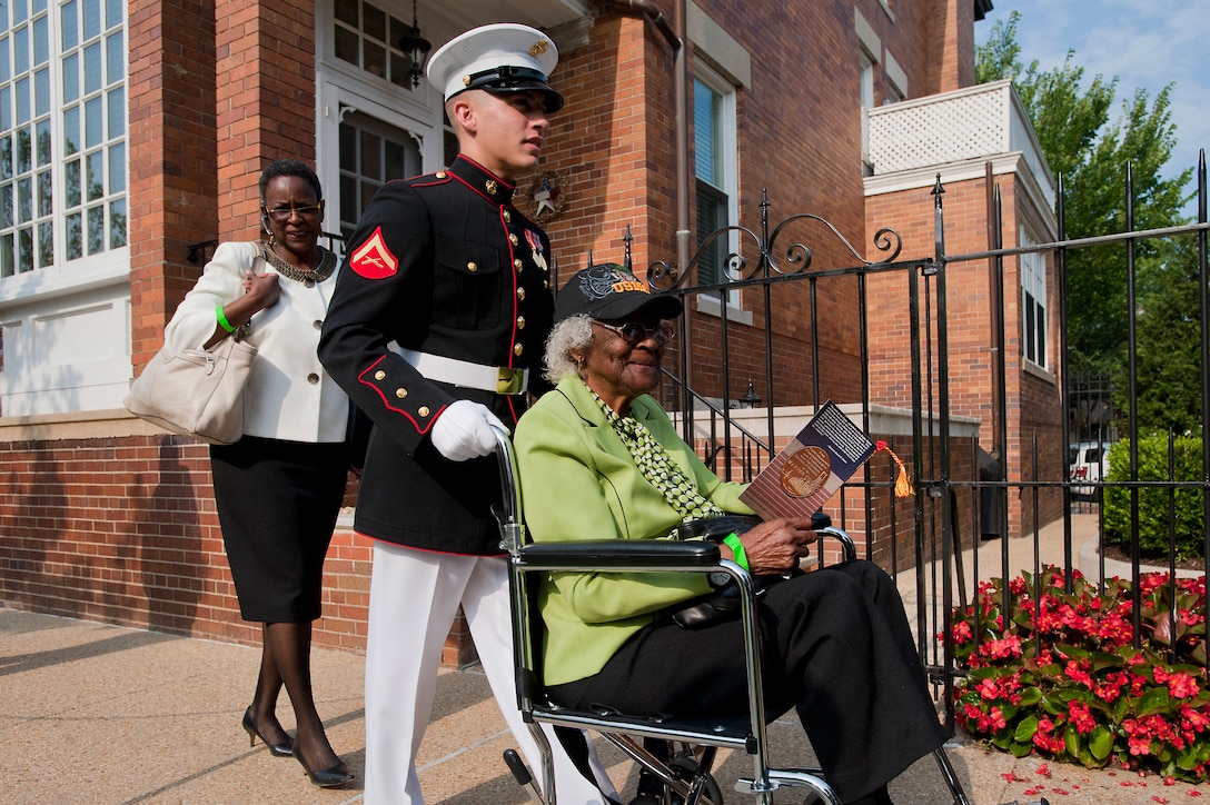 Lance Cpl. Gaige Roberts, Marine Barracks Washington mail room clerk, assists an elderly guest of a Montford Point Marine to her seat before the start of a Congressional Gold Medal ceremony at Marine Barracks Washington June 28. In 1942, President Roosevelt established a presidential directive giving African Americans an opportunity to be recruited into the Marine Corps. Between 1942 and 1949 approximately 20,000 African American Marines received basic training at the segregated Montford Point instead of the traditional boot camps of Parris Island, S.C. and San Diego, Calif. These men fought for their country with honor and valor that are hallmarks of the Corps, but they were not treated as equals to their white counterparts at the time. Gen. James F. Amos, commandant of the Marine Corps, set out to begin to right this wrong when he invited the Montford Point Marines to the Barracks Aug. 26, 2011 to be the guests of honor at a Friday Evening Parade, bringing their story to the national forefront and starting a chain of events that lead to this historic day.