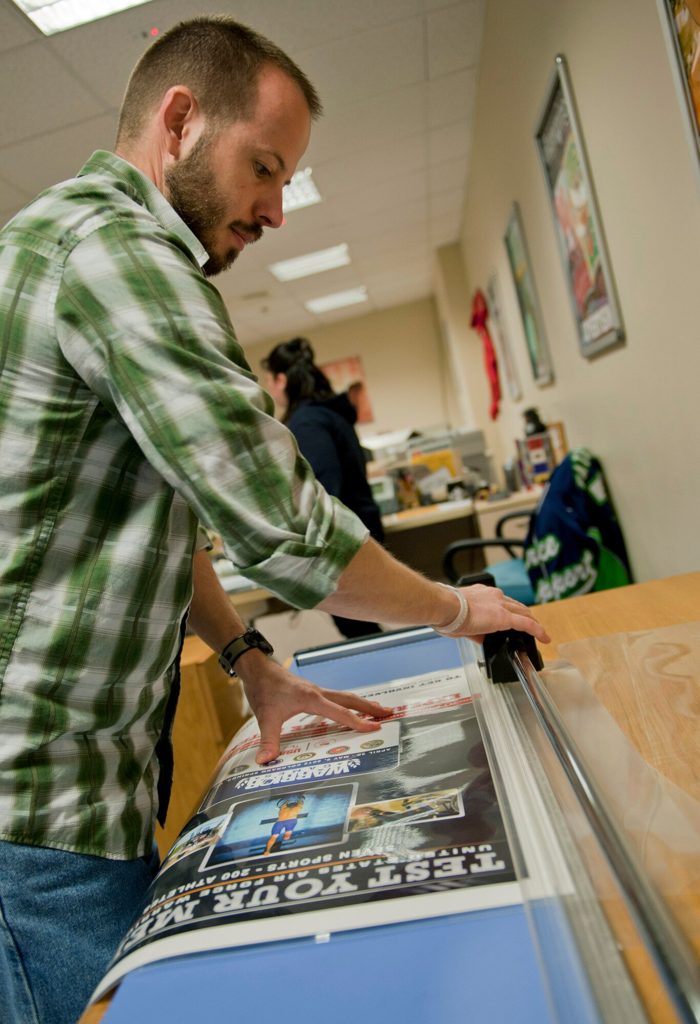 JT McKeen, 39th Force Support Squadron marketing graphic artist, trims the excess laminate off a poster Feb. 29, 2012, at Incirlik Air Base, Turkey. The marketing office creates and prints posters, pamphlets, and other showcase items for the Incirlik community. Marketing also runs the 39th FSS website, blog and Facebook page, sells advertising, and promotes base events. (U.S. Air Force photo by Senior Airman Anthony Sanchelli/Released)
