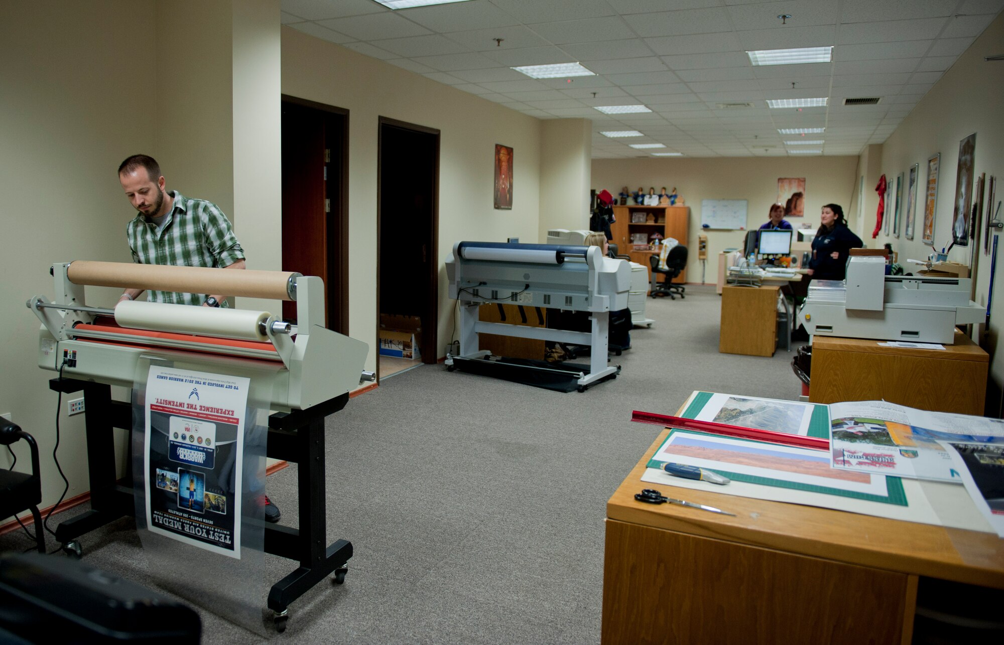 JT McKeen, 39th Force Support Squadron marketing graphic artist, left, laminates a poster Feb. 29, 2012, at Incirlik Air Base, Turkey. The marketing office creates and prints posters, pamphlets, and other showcase items for the Incirlik community. Marketing also runs the 39th FSS website, blog and Facebook page, sells advertising, and promotes base events. (U.S. Air Force photo by Senior Airman Anthony Sanchelli/Released)
