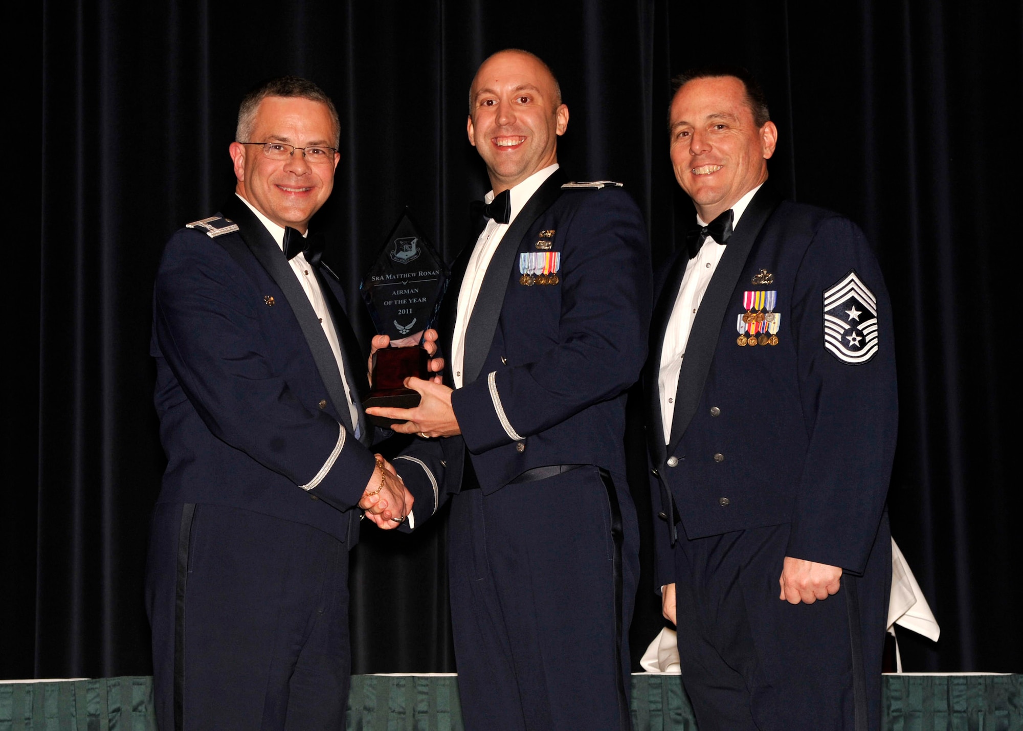Capt. Brian Saul (middle), 512th Logistics Readiness Squadron,  accepts the 512th Airlift Wing 2011 Airman of the Year award on behalf of Senior Airman Matthew Ronan, 512th LRS. The 512th AW revealed all of its annual award winners at a banquet March 3, 2012, at Dover Downs. Also pictured are Col. Randal L. Bright, 512th AW commander, and Chief Master Sgt. William T. Wild III, 512th AW command chief. (U.S. Air Force photo by Tech. Sgt. Chuck Walker)