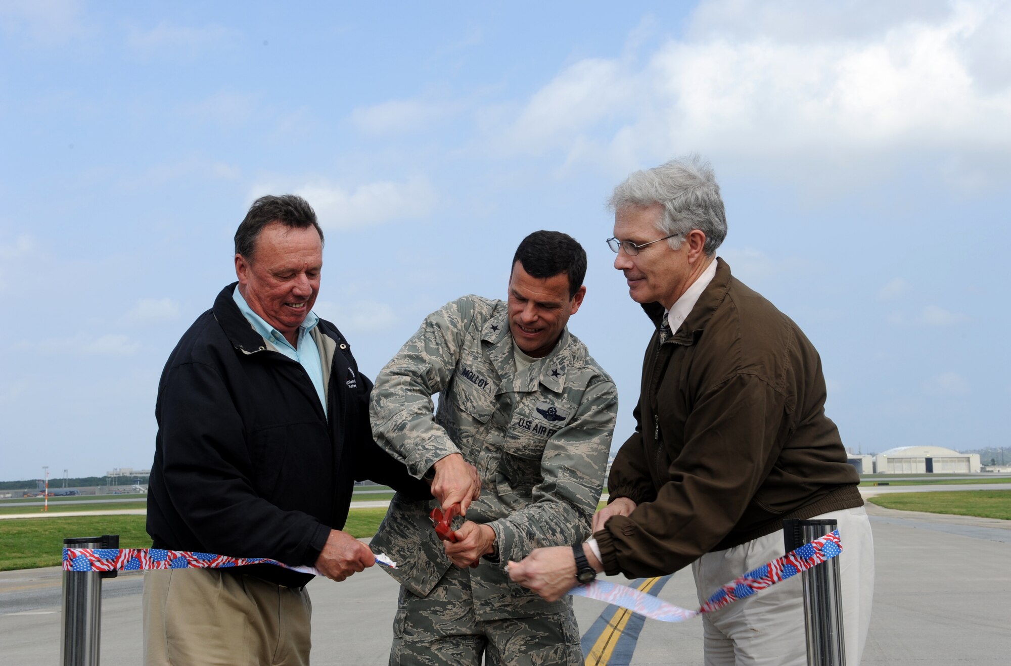 From the left, Brad Williamson, U.S Army Corps of Engineers, Okinawa Area Office quality assurance inspector, Brig. Gen. Matthew Molloy, 18th Wing commander, and Kevin Rogers, 718th Civil Engineer Squadron project manager, cut the ribbon, opening the North runway on Kadena Air Base, Japan, Feb. 29, 2012. The U.S. funded construction project took approximately 18 months to complete and included milling and overlaying existing asphalt pavement, replacing individual concrete pavement slabs and emergency barrier shelters and repairing runway lights and distance-to-go markers. (U.S. Air Force photo by Airman 1st Class Justin Veazie/released) 
