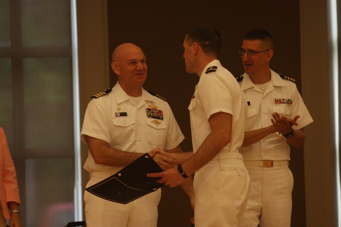 Navy Lt. Mathew Guggenbiller, graduating intern from the Naval Hospital Camp Lejeune Family Medicine Residency program, receives his certificate of completion from Navy Capts. Daniel Zinder, commanding officer of NHCL, and Mark Stephens, associate professor and chair of the Department of Family Medicine, Uniformed Services University of the Health Sciences, during the Family Medicine Residency program graduation at Marston Pavilion aboard Marine Corps Base Camp Lejeune, July 1. The 13 graduating sailors are destined to either continue their training at the hospital or check in at their first duty station as new medical practitioners.