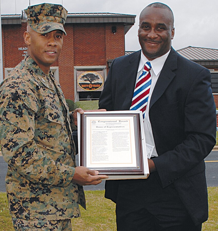 Kenneth Cutts, district director, Office of U.S. Congressman Sanford D. Bishop Jr., 2nd district, D-Georgia, presents a Congressional Record to Col. Terry V. Williams, commanding officer, Marine Corps Logistics Base Albany, during the base’s 60th anniversary at Schmid Field, March 1.