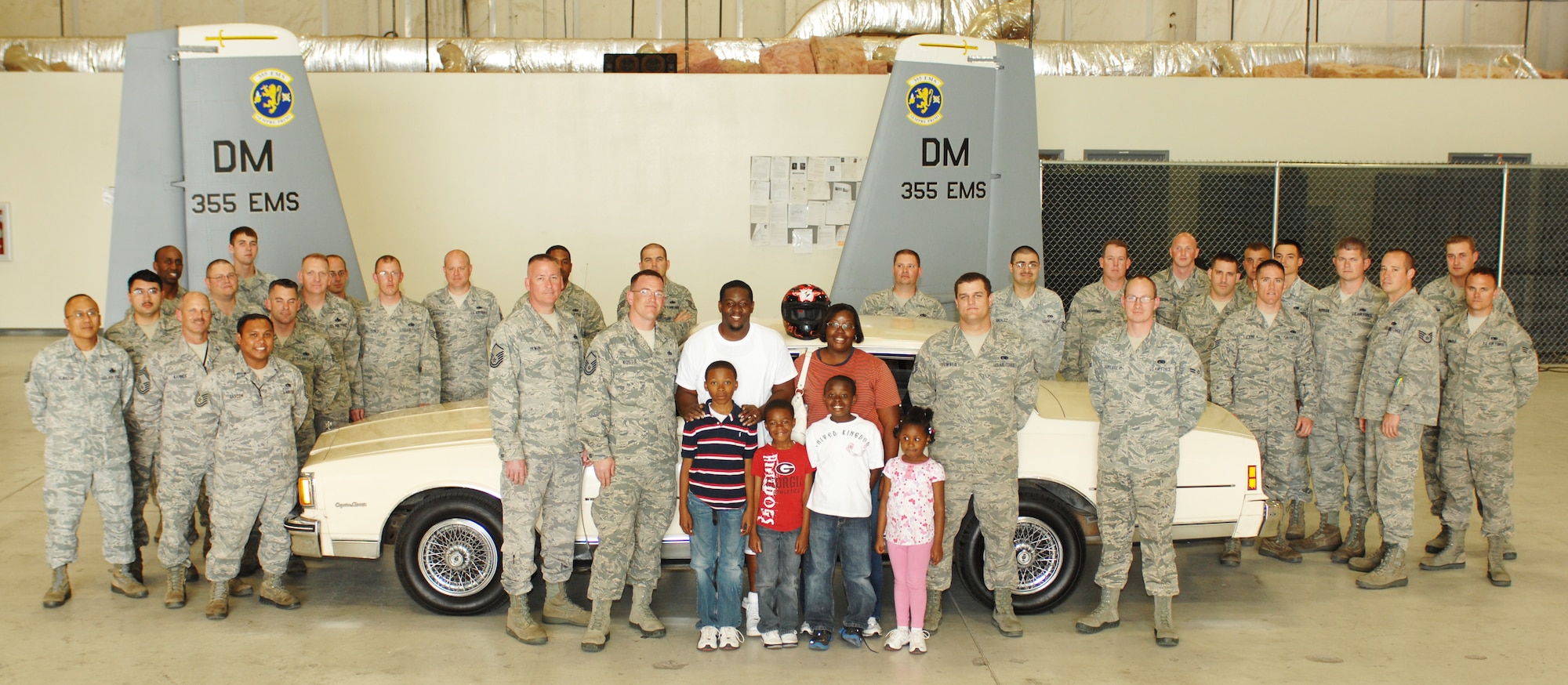 U.S. Air Force Tech. Sgt. Adrian Mapps, 355th Equipment Maintenance Squadron, along with his family and other members of the 355th EMS, stand around Mapps’ restored 1984 Chevy Caprice Classic in a hangar on Davis-Monthan Air Force Base, Ariz., March 5. The car was presented to Mapps by members of his squadron who used their own time and money to refurbish the vehicle after a motorcycle accident totaled Sergeant Mapps’ only working form of transportation. (U.S. Air Force photo by Airman 1st Class Saphfire Cook/Released)