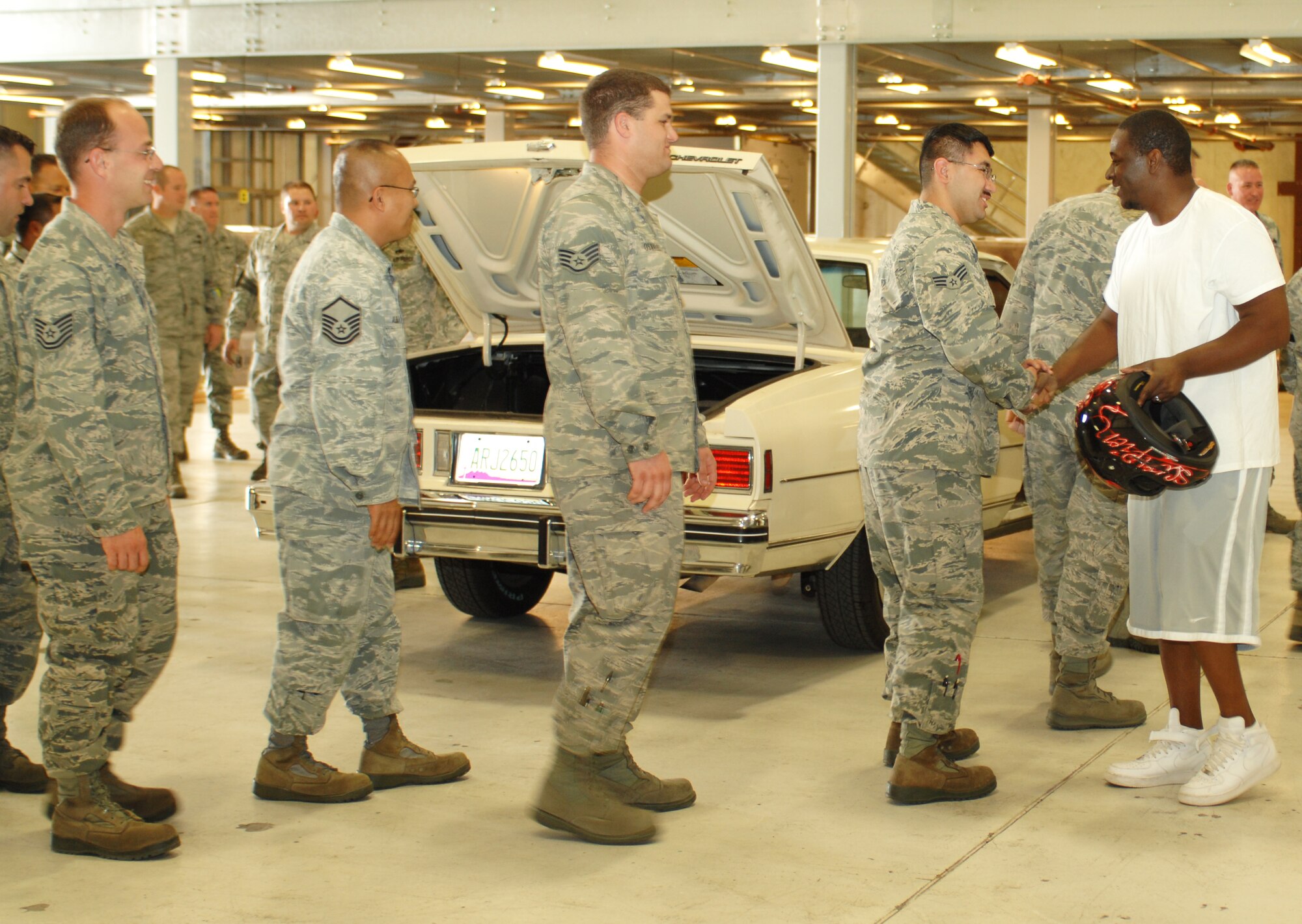 U.S. Air Force Tech. Sgt. Adrian Mapps shakes the hands of his fellow 355th Equipment Maintenance Squadron members after being presented with his restored 1984 Chevy Caprice Classic in a hangar on Davis-Monthan Air Force Base, Ariz., March 5. Mapps was recently involved in a motorcycle accident that totaled his only working form of transportation. Members of his squadron took the non-functioning vehicle from his driveway and repaired it using their own skills and money. (U.S. Air Force photo by Airman 1st Class Saphfire Cook/Released)