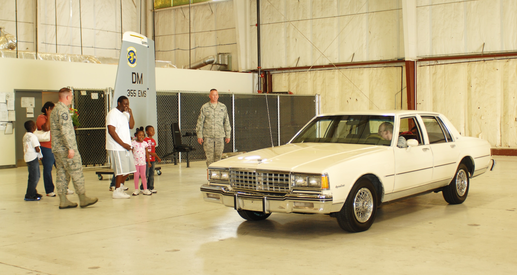 U.S. Air Force Tech. Sgt. Adrian Mapps, 355th Equipment Maintenance Squadron, and his family look on in surprise as the new-and-improved version of their 1984 Chevy Caprice Classic is driven in to the hangar on Davis-Monthan Air Force Base, Ariz., March 5. Members of the 355th EMS pooled their time, money and talents to repair the vehicle for the Mapps family. (U.S. Air Force photo by Airman 1st Class Saphfire Cook/Released)