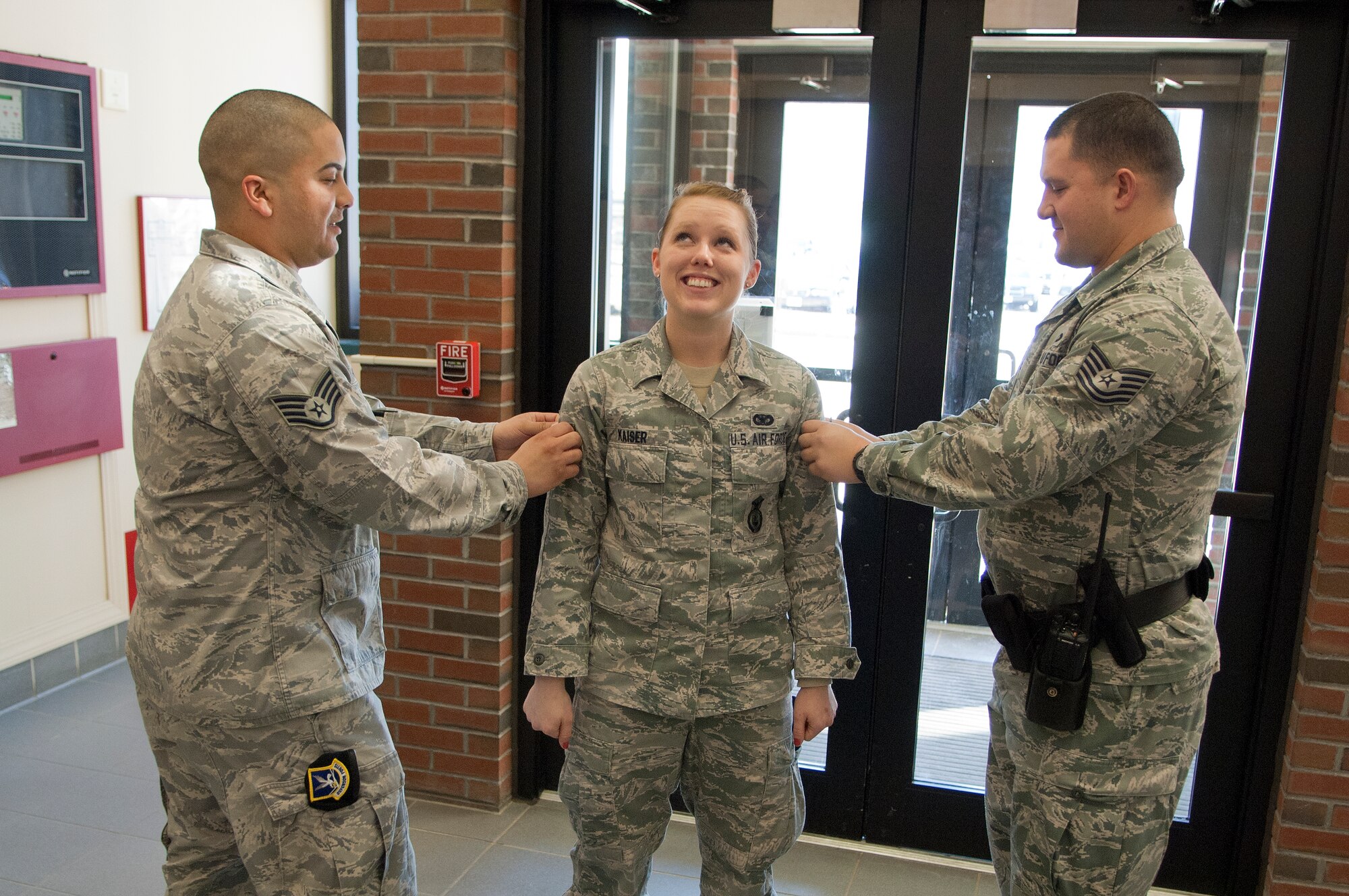 HANSCOM AIR FORCE BASE, Mass. -- Staff. Sgt. Eric Frias (left) and Tech. Sgt. John Mikolaj, both with the 66th Security Forces Squadron, tack on a new stripe for Senior Airman Rebecca Kaiser, 66th Security Forces Squadron pass and registration, in Building 1725 March 7. Kaiser was selected for a Below-the-Zone promotion, allowing her to promote from airman first class to senior airman six months early. (U.S. Air Force photo by Mark Wyatt)