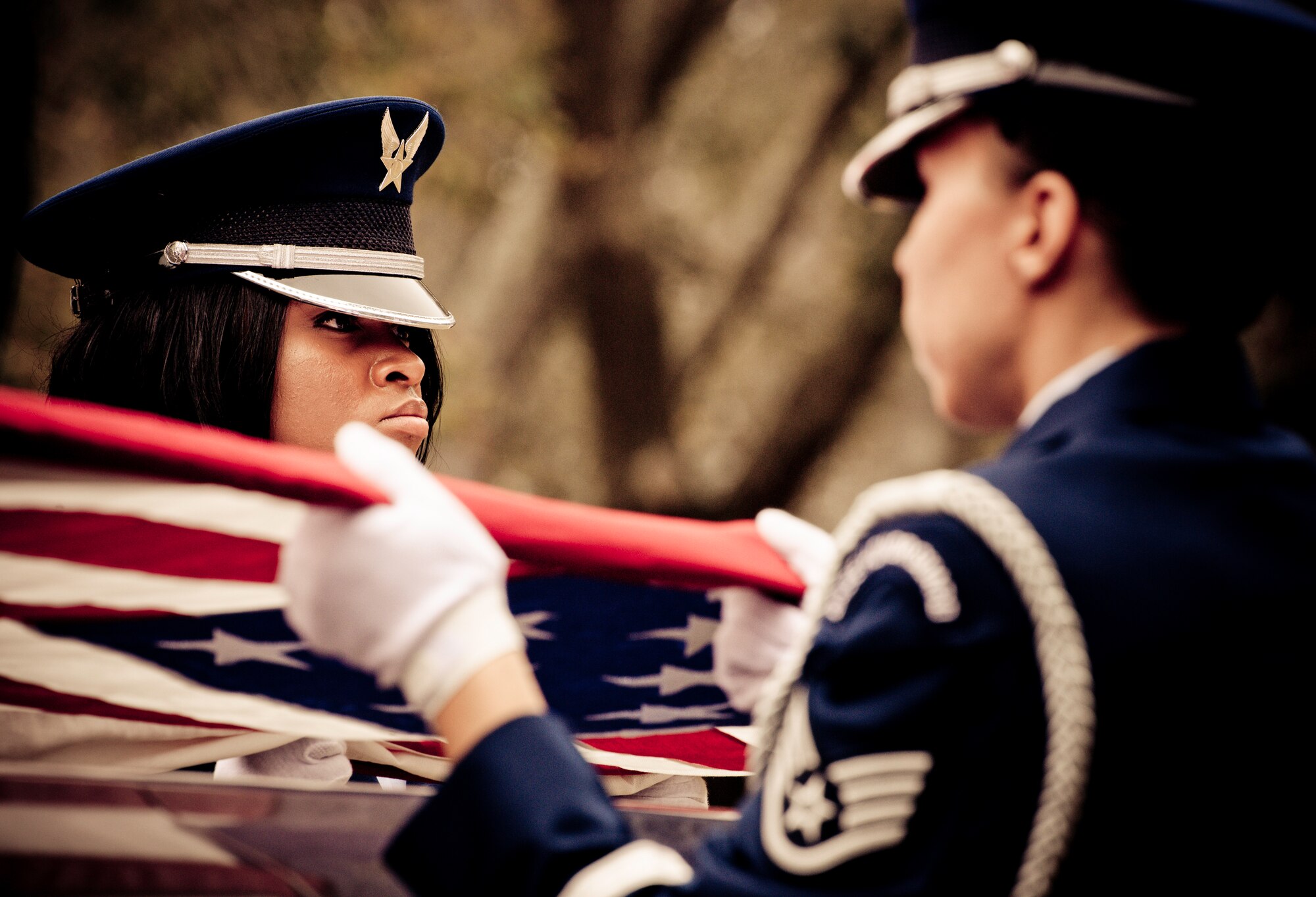 (Left) Airman 1st Class Taurie McCurdy and five other members of the Eglin Honor Guard hold the flag tight above the casket during a mock funeral as part of the honor guard graduation. Approximately 16 new Airmen graduated from the 80-plus-hour course.  Prior to the graduation, the Airmen perform a full honors, military funeral to include flag detail, the 21-gun salute, pall bearers and bugler for friends, family and unit commanders.  (U.S. Air Force photo/Samuel King Jr.)