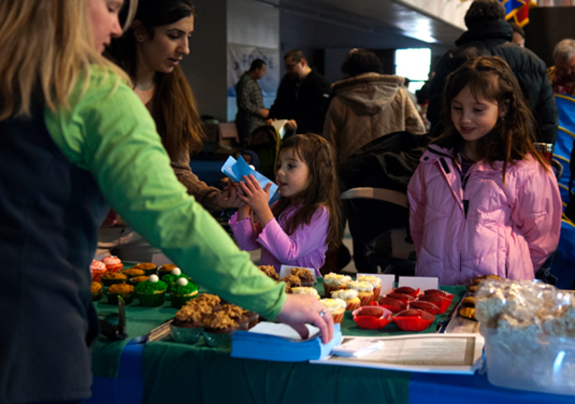 Sevgi Norman buys baked goods for her daughters, Aleyna, 4, and Melissa, 8, at Robin Midlam’s booth in Fall Hall Community Center March 3. Midlam said she spent two days baking in preparation for the flea market. (U.S. Air Force photo by R.J. Oriez)