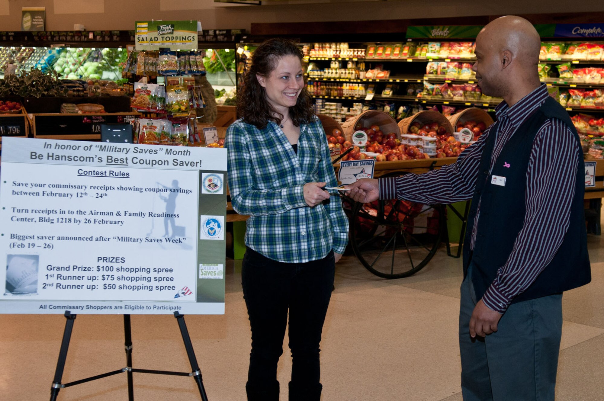 HANSCOM AIR FORCE BASE, Mass. – Commissary administrator Anthony Gardner hands Brandy Kovacic a check for a $100 shopping spree after she won the grand prize in Hanscom’s best coupon saver competition. The contest was a part of Military Saves Week, which is an annual Air Force-wide savings and debt reduction campaign. (U.S. Air Force Photo by Rick Berry)