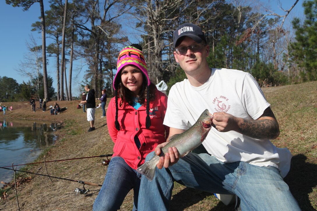 Cpl. Joshua Bachand, a rifleman with 3rd Battalion, 9th Marine Regiment, 2nd Marine Division, and his step daughter hold up a rainbow trout, which was the first fish caught during the Family Fun Fishing event, March 10. The pond was stocked with approximately 400 pounds of striped bass and rainbow trout that came from a local fish farm.