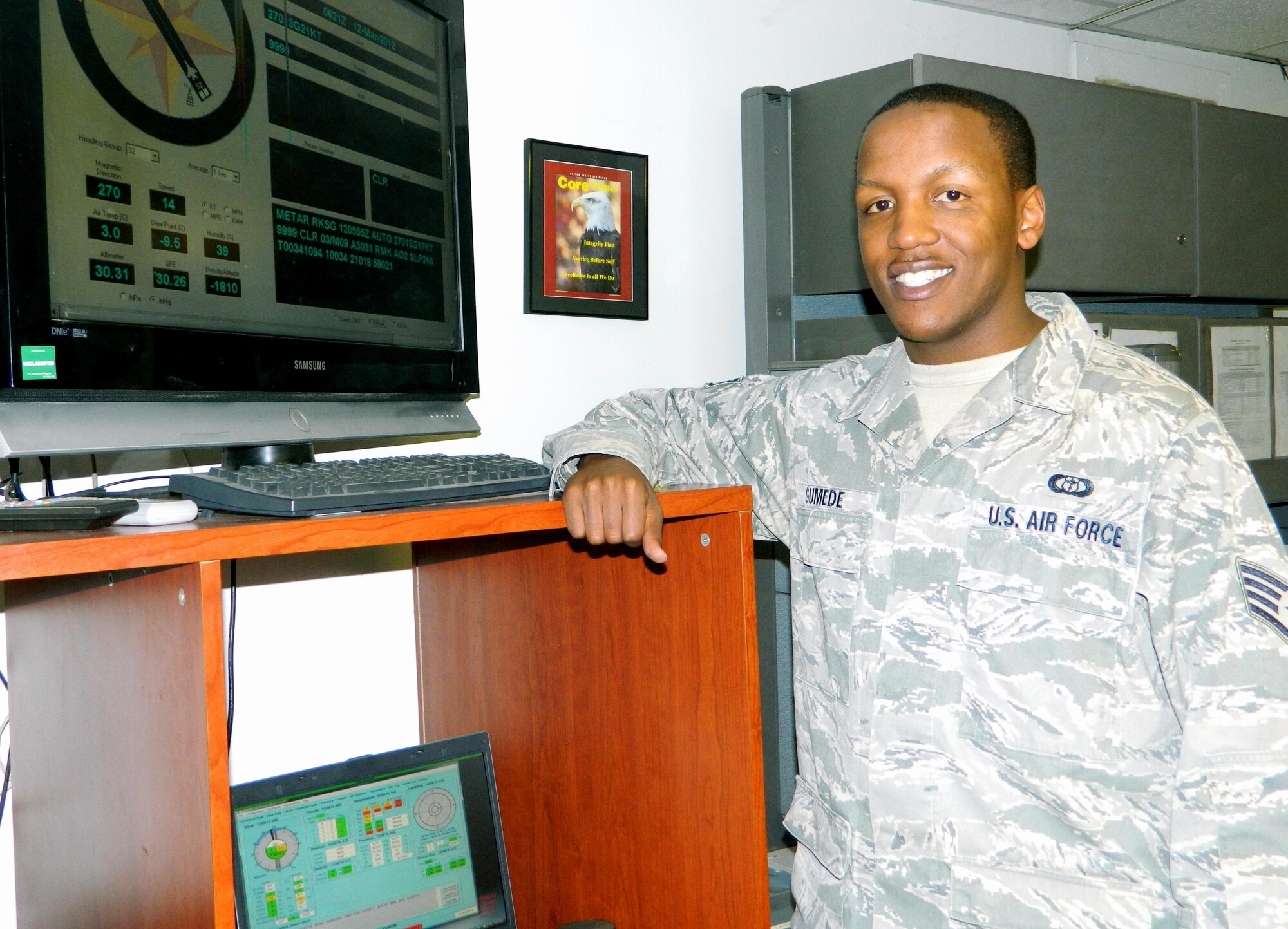 SSgt Gumede standing in front of the Automated Weather Observing System readout while augmenting the observation.  