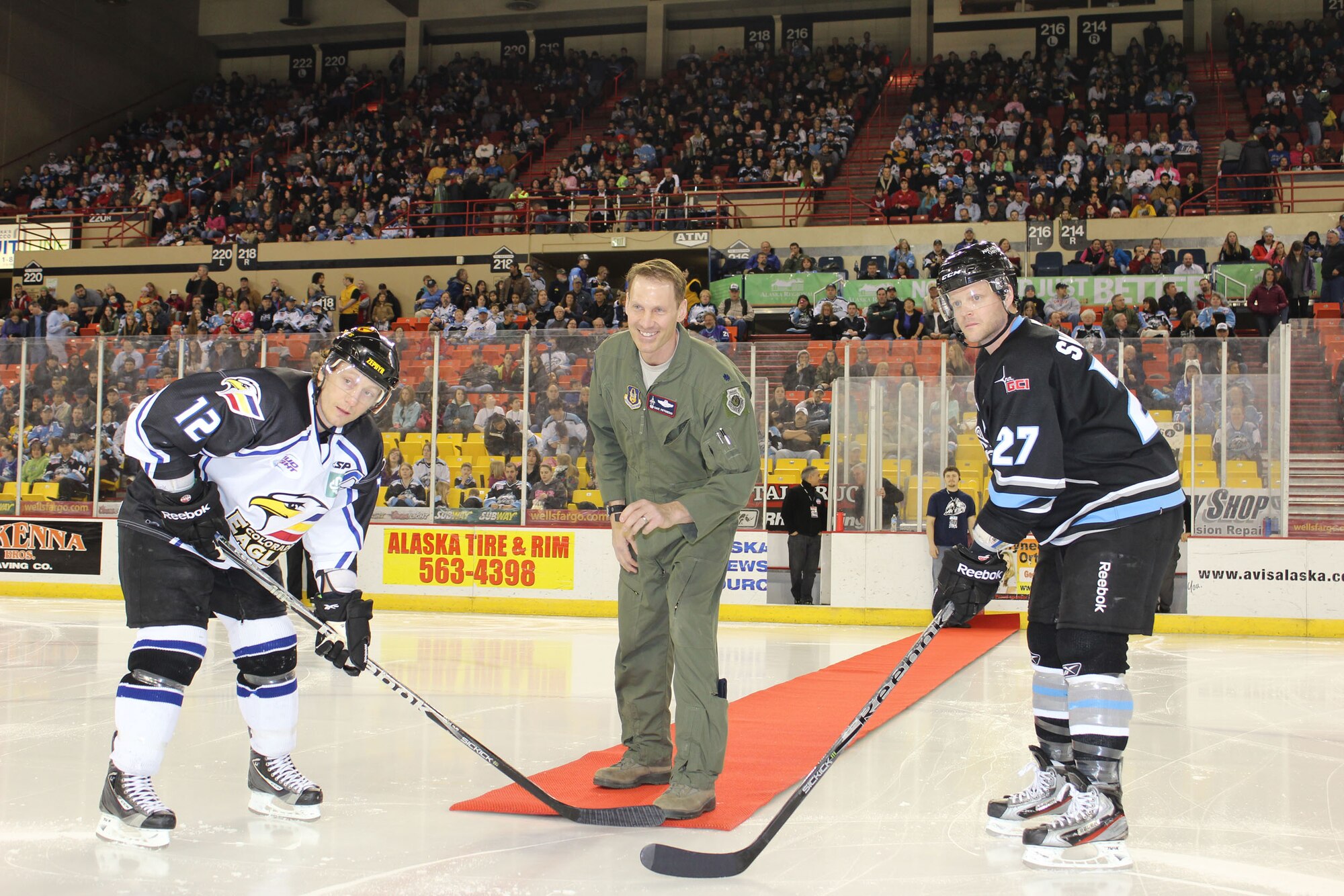 Lt. Col. David Piffarerio, 302nd Fighter Squadron commander, drops the puck between Alaska Aces Team Captain Brian Swanson and Colorado Eagles Team Captain Riley Nelson before the Alaska Aces game March 10. Before the puck drop Piffarerio thanked spectators in attendance for supporting the F-22 and the Air Force Reserve in Alaska. (U.S. Air Force/ Tech. Sgt. Dana Rosso) 