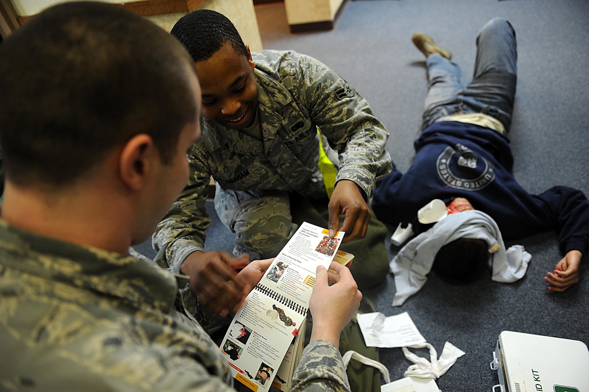 U.S. Air Force Airman 1st Class Tyler Matthews and Charlie Graham, 18th Logistics Readiness Squadron, go through an Airman's Manuel to make sure they are helping the simulated victim properly and effectively on Kadena Air Base, March 12, 2012. Local operational readiness exercises give Airmen the opportunity to train in a safe environment and prepare for real world contingencies. (U.S. Air Force photo by Airman 1st Class Brooke P. Beers/Released)
