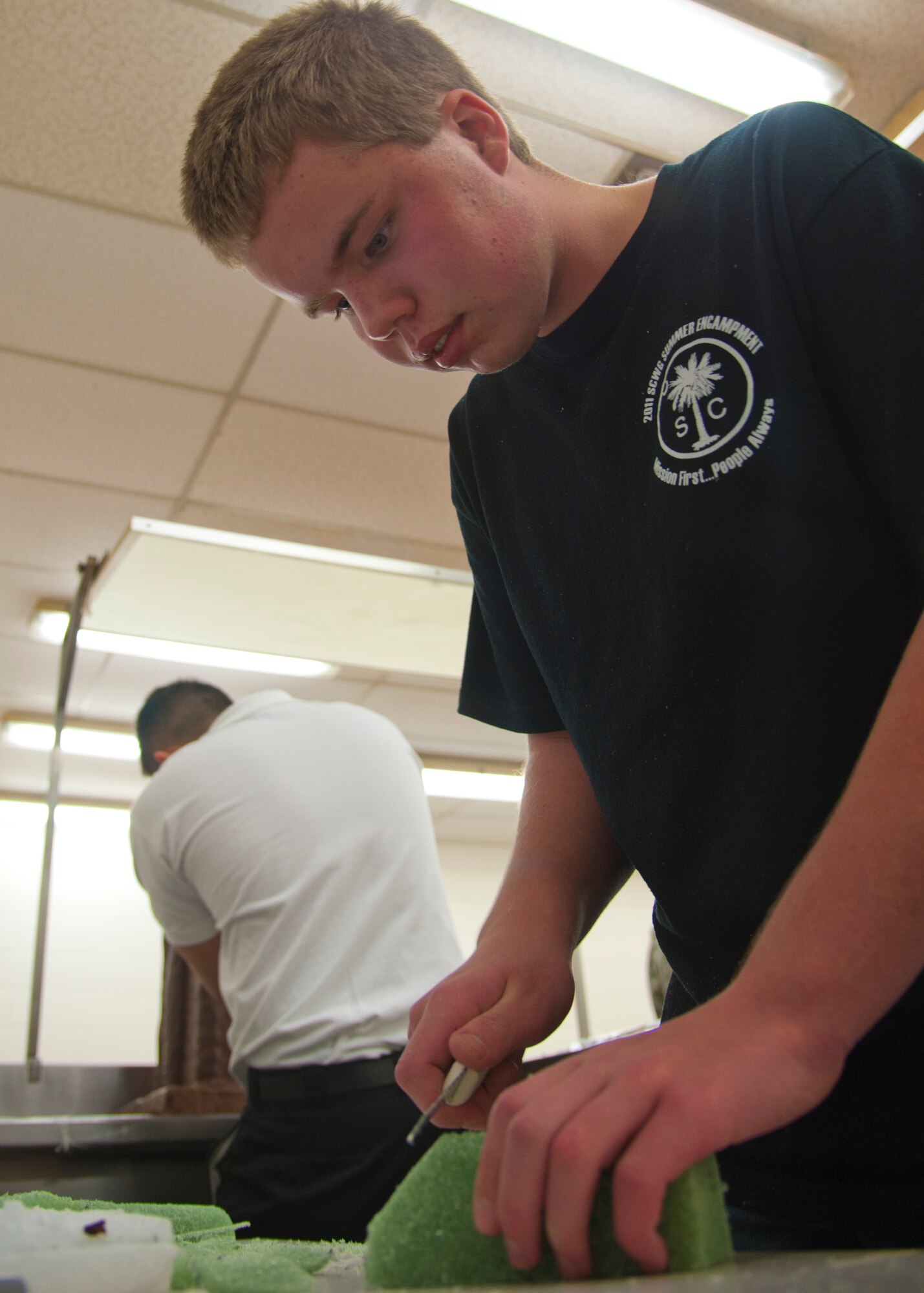 Adam Eudy, a 16-year-old student from South Carolina, slices craft foam to use as structural support for the Joint Base Langley-Eustis Culinary Arts Team showpiece during the 37th Annual Military Culinary Arts Competition at the Joint Culinary Center of Excellence at Fort Lee, Va., Mar. 5. Adam was tutored by the JBLE team to further his skills towards becoming a master chef. (U.S. Air Force photo by Senior Airman John Strong/ Released)