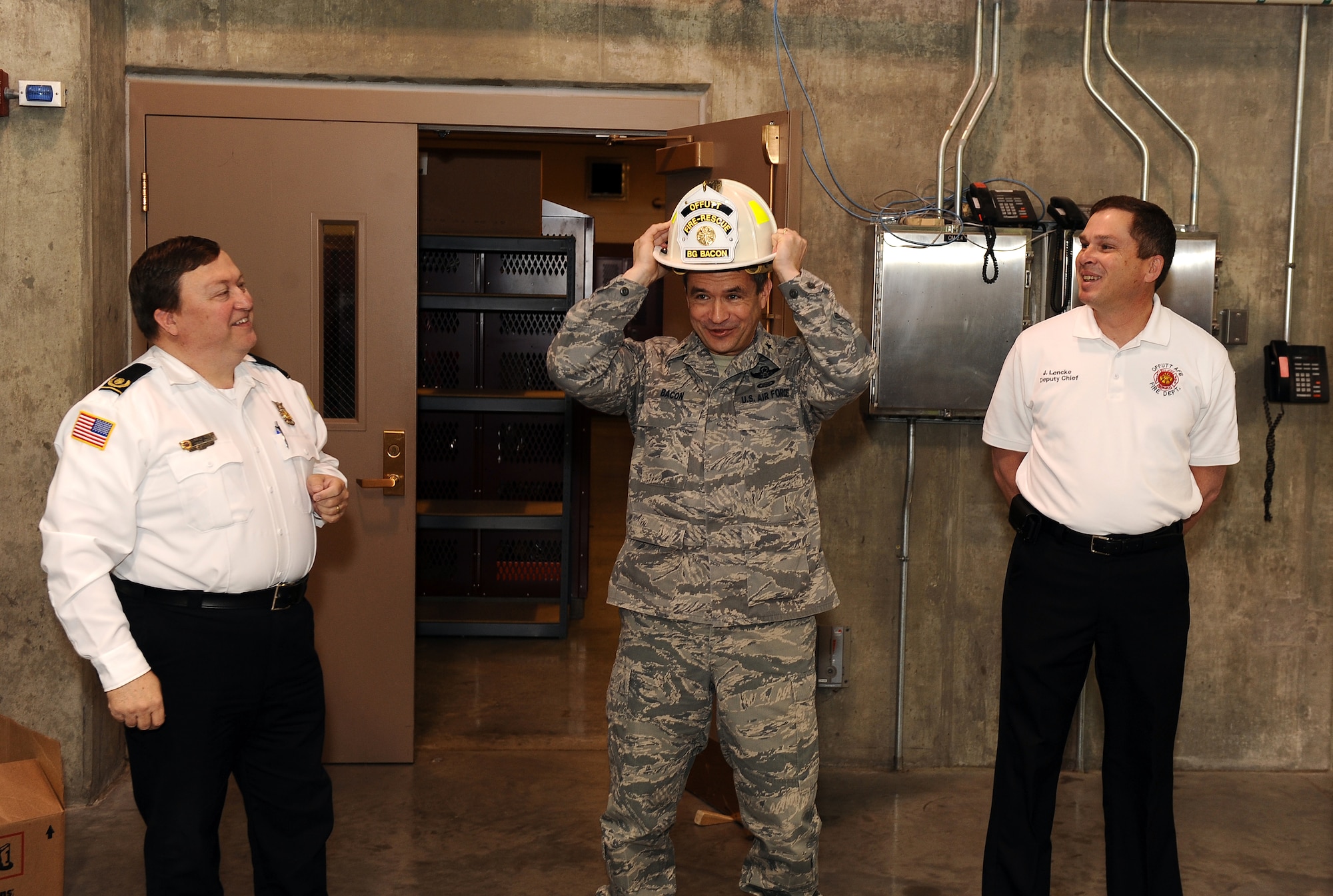 U.S. Air Force Brig Gen. Donald Bacon, 55th Wing commander, places his honorary fireman's hat on his head during morning roll call at the Offutt Air Force Base firehouse, Neb., March 8.  Offutt Fire Chief David Eblin (left) and deputy fire chief James Lencke (right) honored Bacon with a gift following his 24-hour shift training with Offutt's fire fighters.  (U.S. Air Force photo by Josh Plueger/Released).