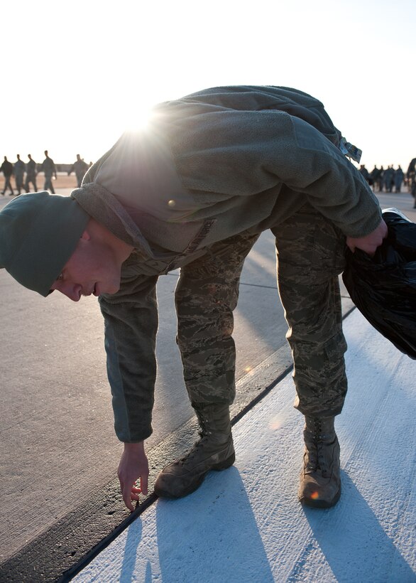 Airman 1st Class Patrick Garrett, 28th Civil Engineer Squadron electrical technician, picks up a rock during a foreign object and debris walk on Ellsworth Air Force Base, S.D., March 12, 2012. Even the smallest rock or piece of wire left on the flightline can potentially cause millions of dollars worth of damage to aircraft engines. (U.S. Air Force photo by Airman 1st Class Alystria Maurer/Released)