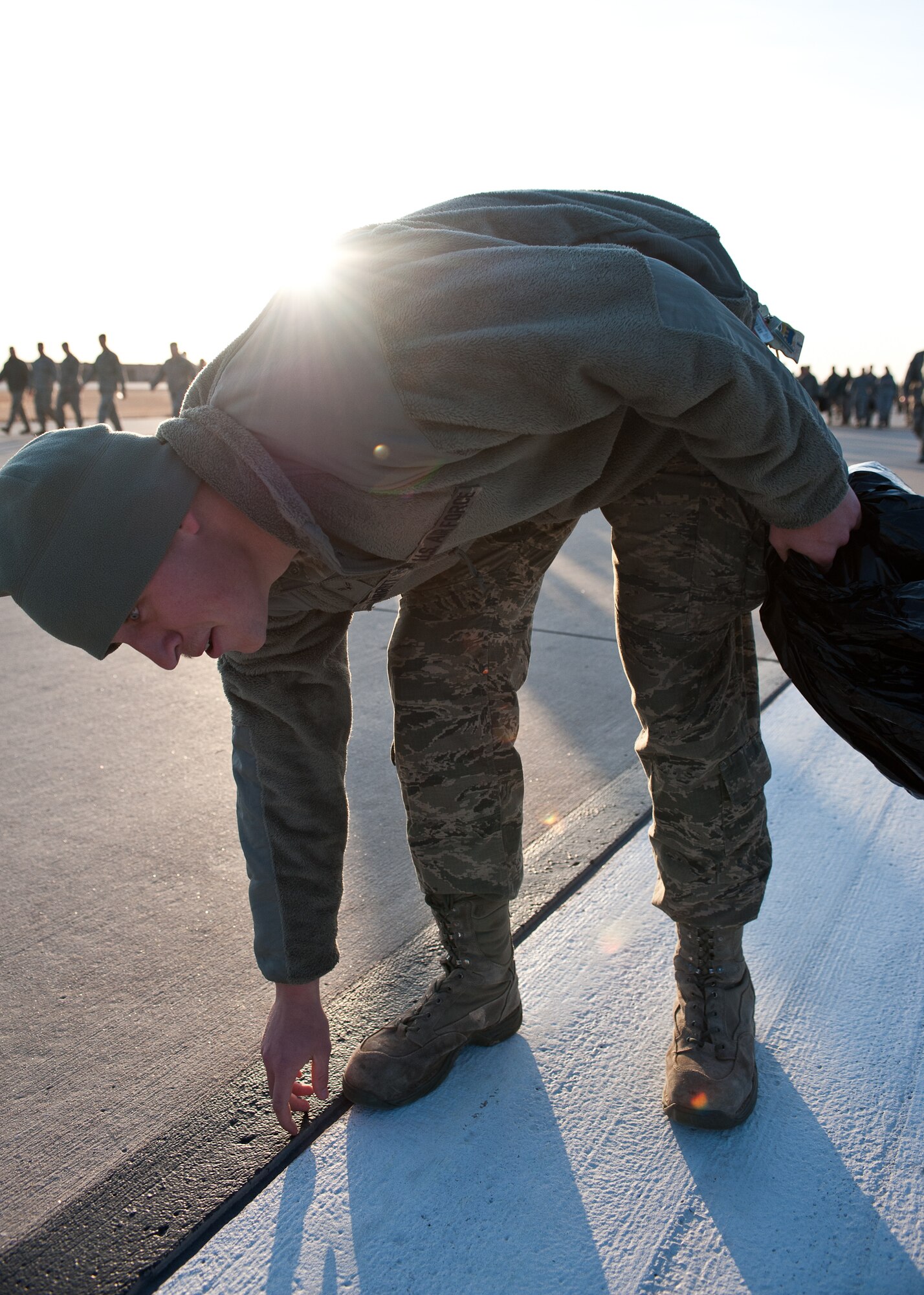 Airman 1st Class Patrick Garrett, 28th Civil Engineer Squadron electrical technician, picks up a rock during a foreign object and debris walk on Ellsworth Air Force Base, S.D., March 12, 2012. Even the smallest rock or piece of wire left on the flightline can potentially cause millions of dollars worth of damage to aircraft engines. (U.S. Air Force photo by Airman 1st Class Alystria Maurer/Released)