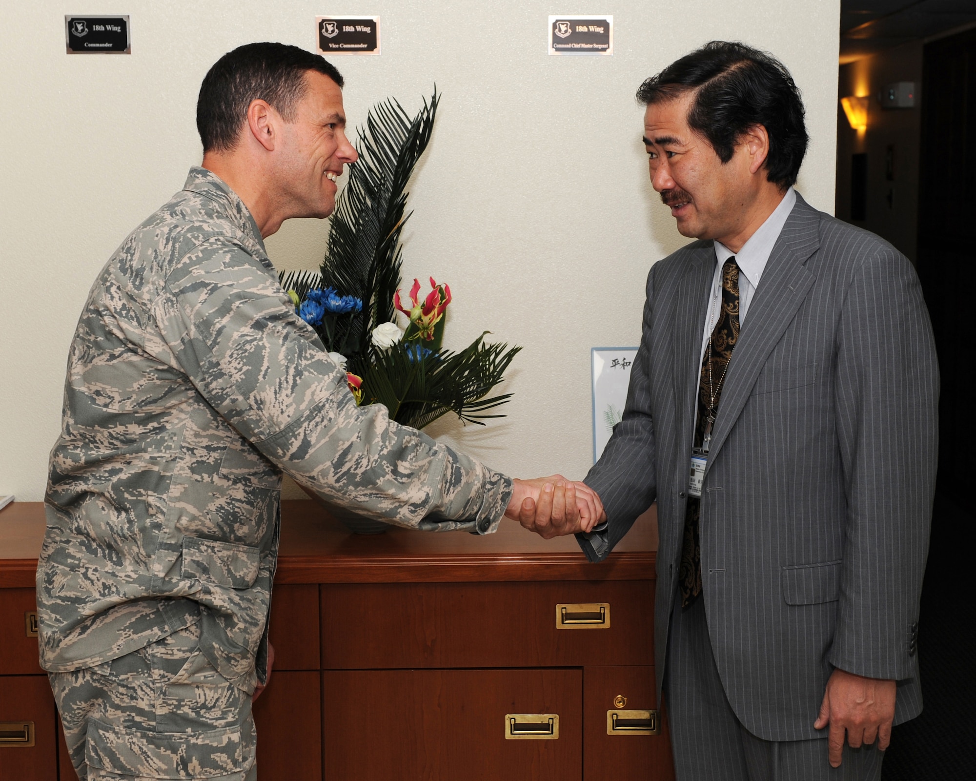 U.S. Air Force Brig. Gen. Matthew Molloy, 18th Wing commander, shows appreciation for a flower arrangement demonstration and presents coin to Mr. Kingo Ikeda, Okinawa Defense Bureau Public Affairs chief, during his visit to Kadena Air Base, Japan, March 14, 2012. The title of his ikebana arrangements is “Wing of Peace”, using an Okinawa local plant called sotetsu and the color coordination to represent the American colors. (U.S. Air Force photo by Junko Kinjo/Released)