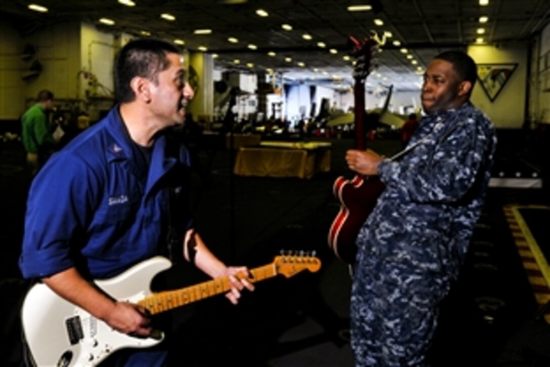 Navy Petty Officers 3rd Class  Robert Saaga, left, and Enyiomadi Chuta, right, play guitar in the hangar bay of the USS Carl Vinson, March 13, 2012, as part of a celebration marking the 30th anniversary of the ship's commissioning. The ship is under way in the Arabian Sea. 