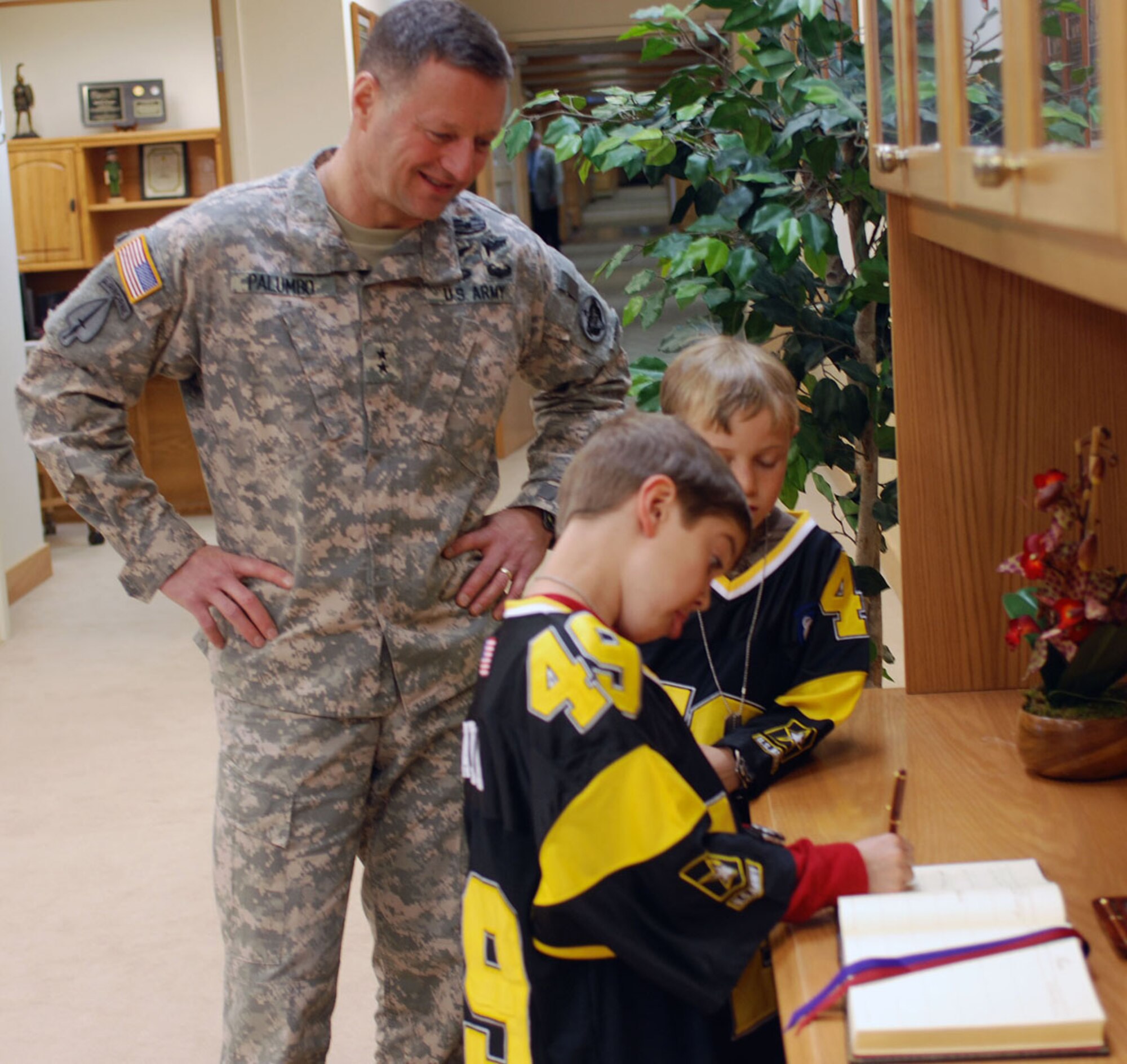 Nathan Rothe and Collin Prokasy are invited by Maj. Gen. Raymond Palumbo, U.S. Army Alaska Commander, to sign the official USARAK visitor?s book, recording them as honored guests to the command and marking Nathan?s time as a Soldier for a day. Nathan, who has muscular dystrophy and lives in Dallas, is visiting Alaska to experience an arctic winter. (Photo by Staff Sgt. Matthew E. Winstead/U.S. Army Alaska Public Affairs)