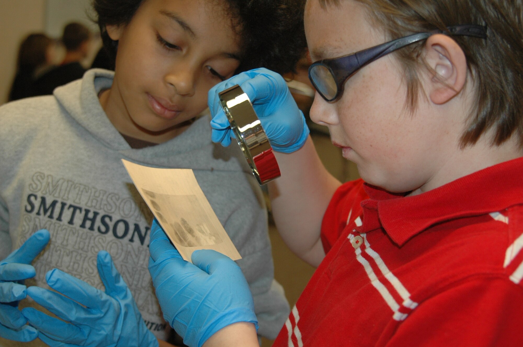 Logan Riley, a sixth-grade student from Travis Elementary School, examine finger prints using a magnifier during the mock investigation held Monday in the school’s music room. (U.S. Air Force photo/ Tyler Grimes) 