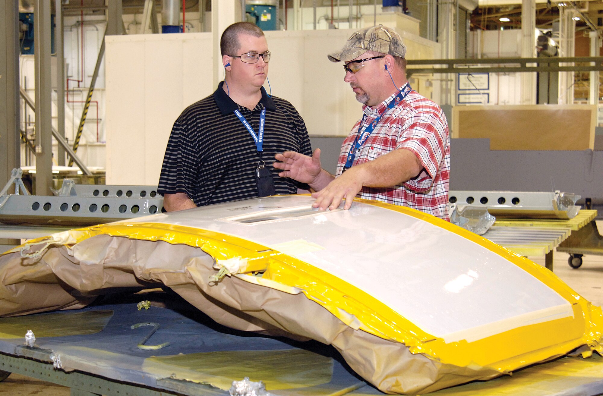 Paint shop supervisor Anthony Hunt, left, and paint work leader Scott Sawyer discuss processes beside a painted and stenciled E-3 entry door in the 551st Commodities Maintenance Squadron paint shop located in Bldg. 9001. Personnel of the shop adopted a modular work flow that soared production numbers, chopped production days and keeps reaping benefits for the shop and their customers basewide. (Air Force photos by Margo Wright)