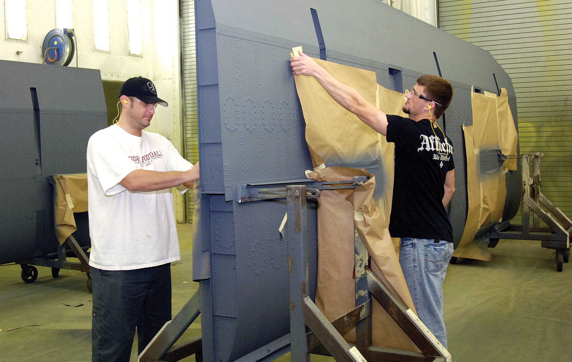 Removing masking from a B-52 flap after painting in a 551st Commodities Maintenance Squadron booth are painters Kevin Millian, left, and Dillon Johnson.  The shop, located in Bldg. 9001, paints parts for every airframe Tinker maintains and a new shop workflow is speeding those parts back to shops across base in record time. (Air Force photos by Margo Wright)