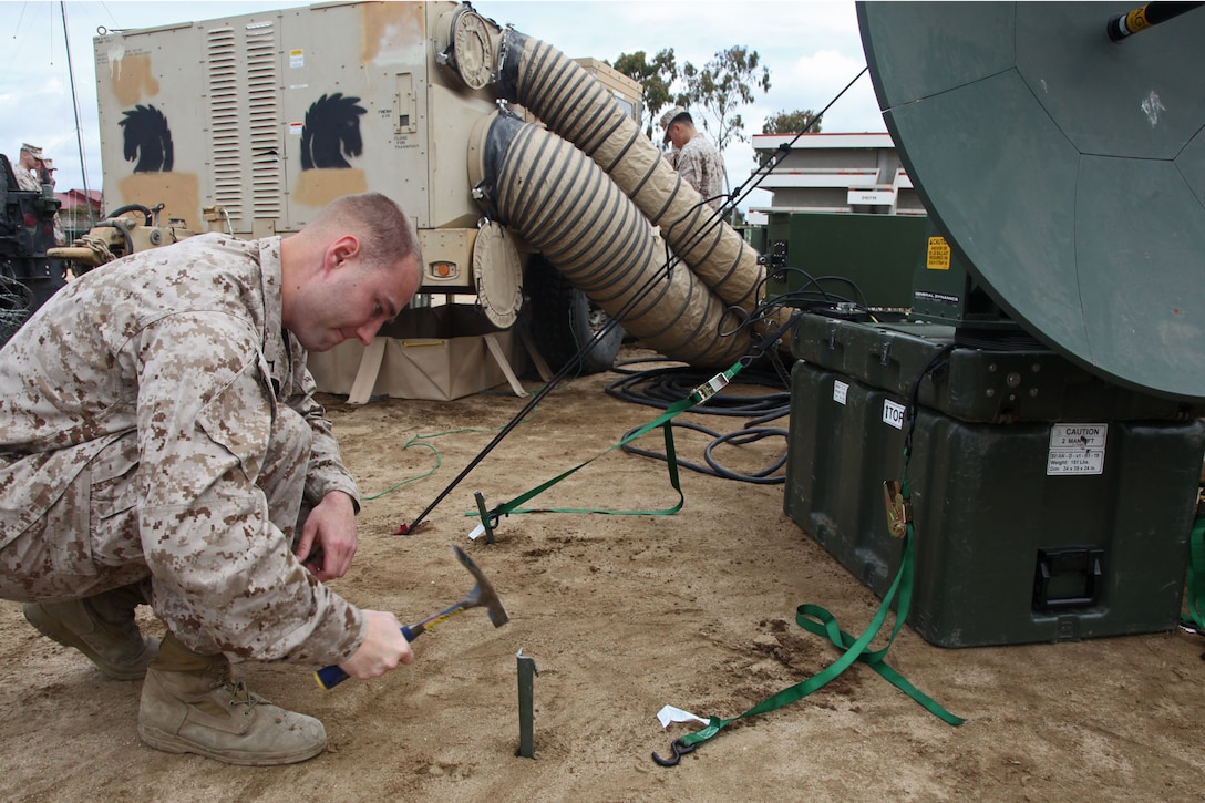 Pfc. Christopher S. Lafriniere, data communications specialist, Battalion Landing Team 3/5, 15th Marine Expeditionary Unit, drives a stake to secure a Support Wide Area Network satellite during a Communications Exercise with the entire Marine Air Ground Task Force at Camp Delmar, March 19. The five-day training exercise is meant to prepare the 15th MEU for a deployment qualification exercise in the coming future.