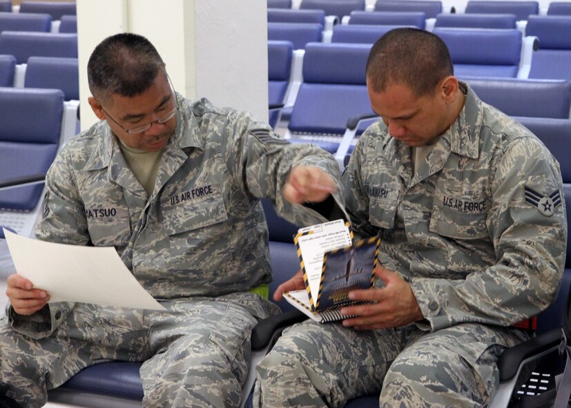 Tech. Sgt. Glenn Matsuo, 48th APS ramp operations, checks Senior Airman Isaiah Laikupu’s Airman’s Manual for updates to the instruction. As real-world responses evolve, the Air Force sends revised sections on adhesive paper, so Airmen can stick the latest instruction into the manual. (U.S. Air Force photo/Master Sgt. Peter Rieta)