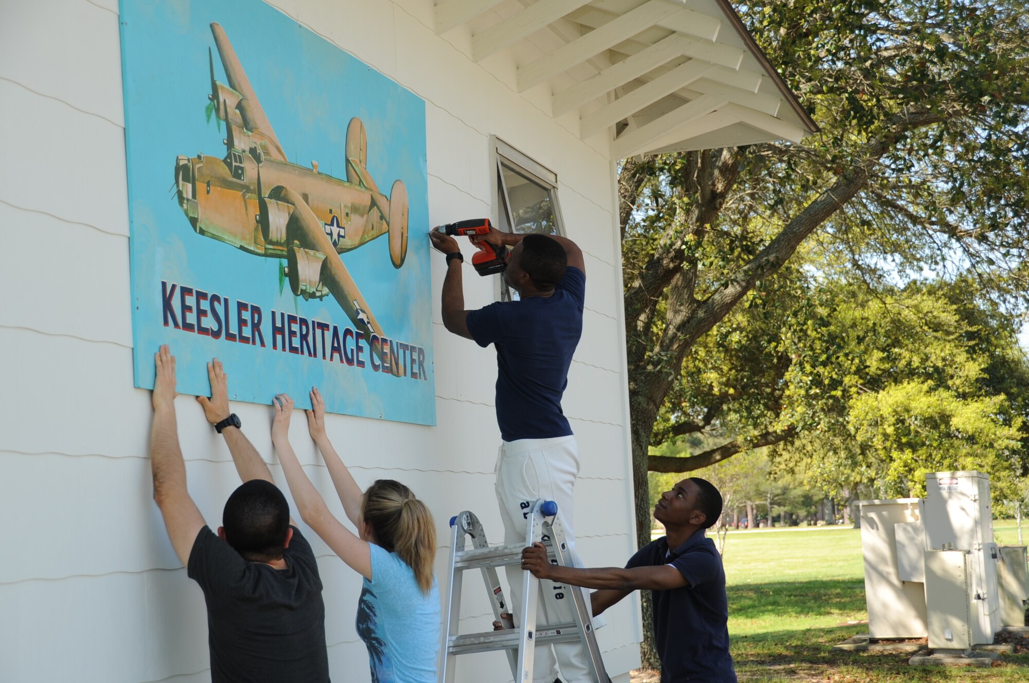 Airmen 1st Class Ricardo Solis and Jamie Ogeda; Airman Basic Nichola Moore; and Airman 1st Class Ja’Mario Powell, 334th Training Squadron, hang the Keesler Heritage Center sign on the building on Meadows Drive March 16, 2012, Keesler Air Force Base, Miss.  The building was built in the 1940s and was originally used as a barracks.  Over time it was used as offices and most recently a functioning Heritage Center until Hurricane Katrina damaged the building in 2005.  The Keesler Heritage Center was renovated on the outside in 2011.   Forty-Five students and staff from the 334th TRS volunteered to renovate the inside of the building by filing photos, cleaning the rooms, disassembling old shelving, taking out trash, and organizing rooms and putting together displays.  (U.S. Air Force photo by Kemberly Groue)