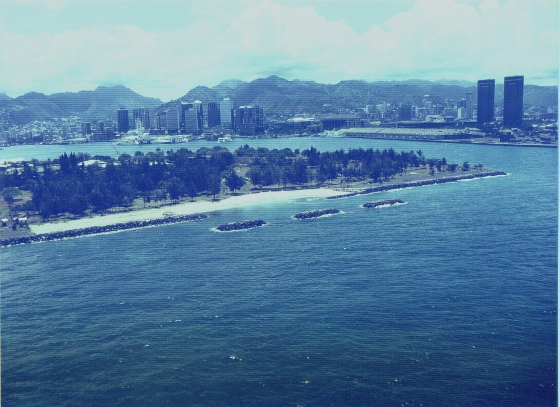 Offshore photograph of the Sand Island shore protection project on the island of Oahu. The three 70-foot long breakwaters are shown in the foreground fronting the completed shoreline revetments totaling 3,962 feet. 
