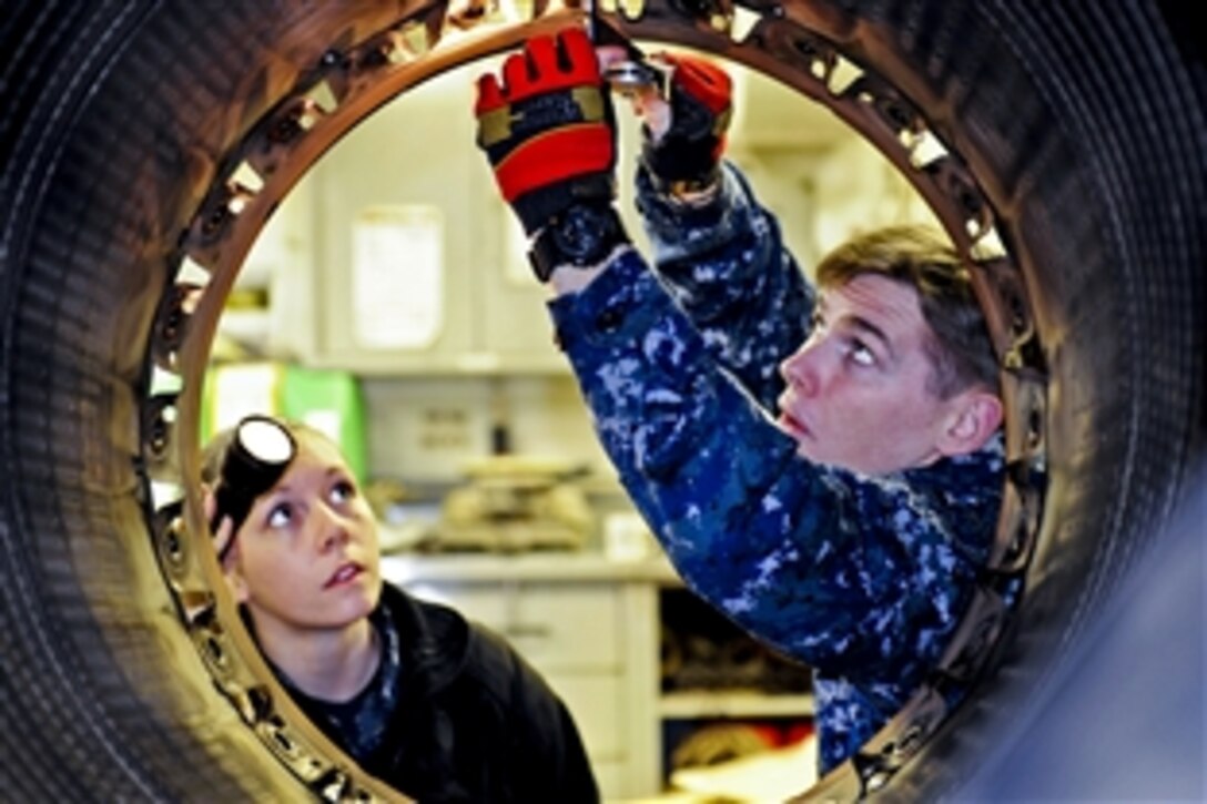 Navy Seamans Michael Walsh, right, and Chandra Tremayne perform maintenance on a 404-400 jet engine afterburner aboard the aircraft carrier USS Nimitz in Everett, Wash., March 19, 2012. Walsh and Tremayne are aviation machinist's mates airmen. The engine components will be used on an F-18 Legacy aircraft. Nimitz recently arrived to its new homeport of Everett.