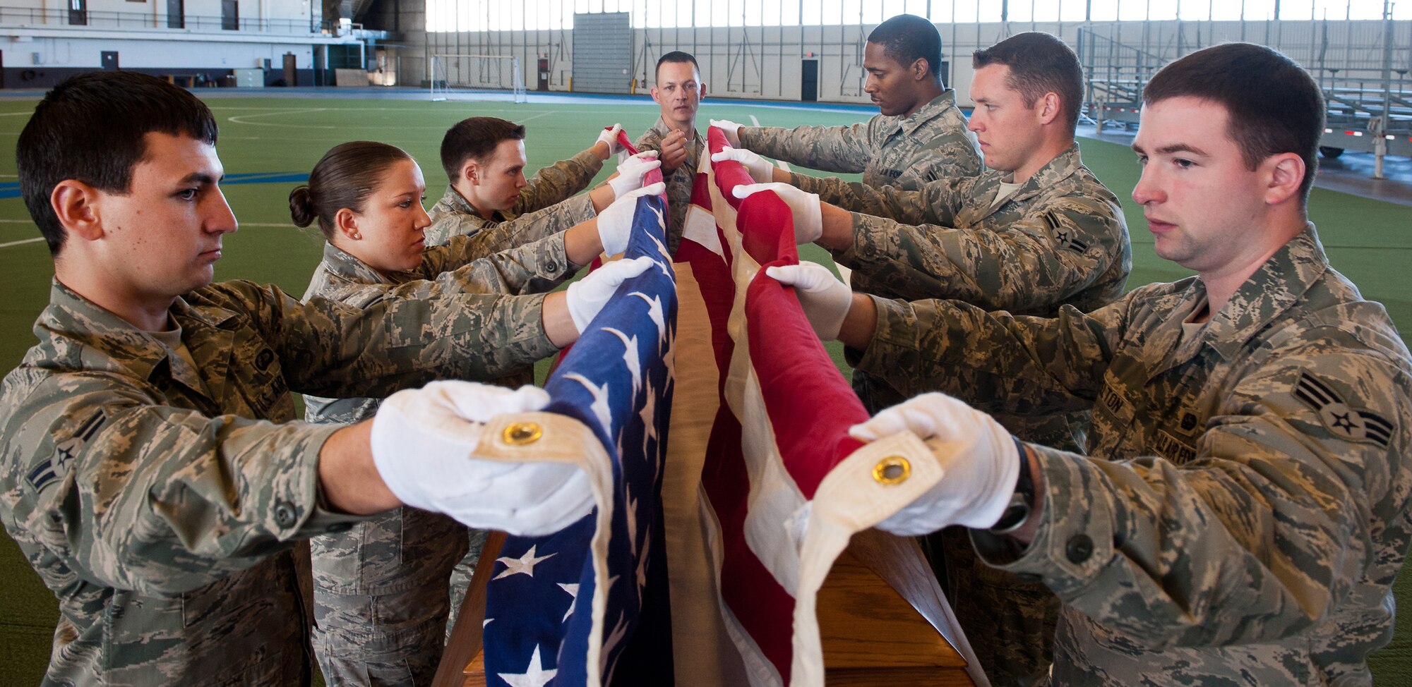 Ellsworth Honor Guard members practice folding a U.S. flag under the watchful eye of Tech. Sgt. Michael Lewis, NCO in charge of the Ellsworth Honor Guard, during a funeral practice sequence in the Pride Hangar at Ellsworth Air Force Base, S.D., March 19, 2012. The base honor guard pays tribute to those who have served the nation by performing a variety of military honors for active-duty servicemembers and U.S. military retirees. (U.S. Air Force photo by Airman 1st Class Kate Thornton/Released)