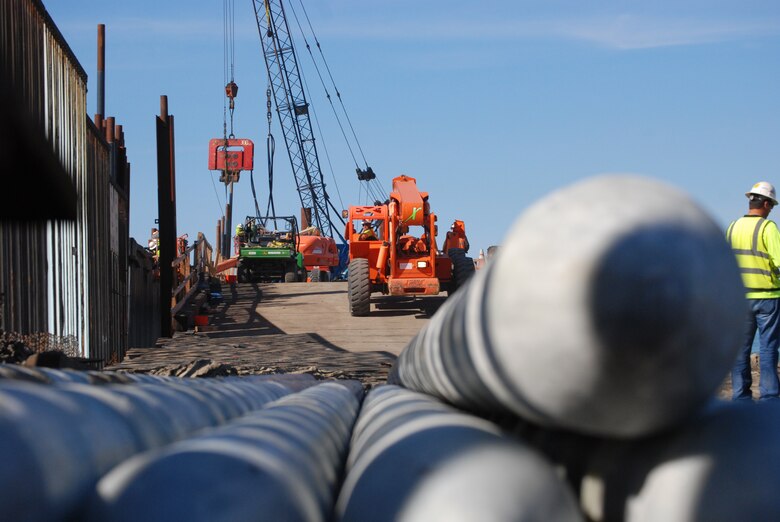 Pilings for the border fence lay at the foot of the temporary pier awaiting their turn to be hauled to the crane that will drive them into the ocean floor below