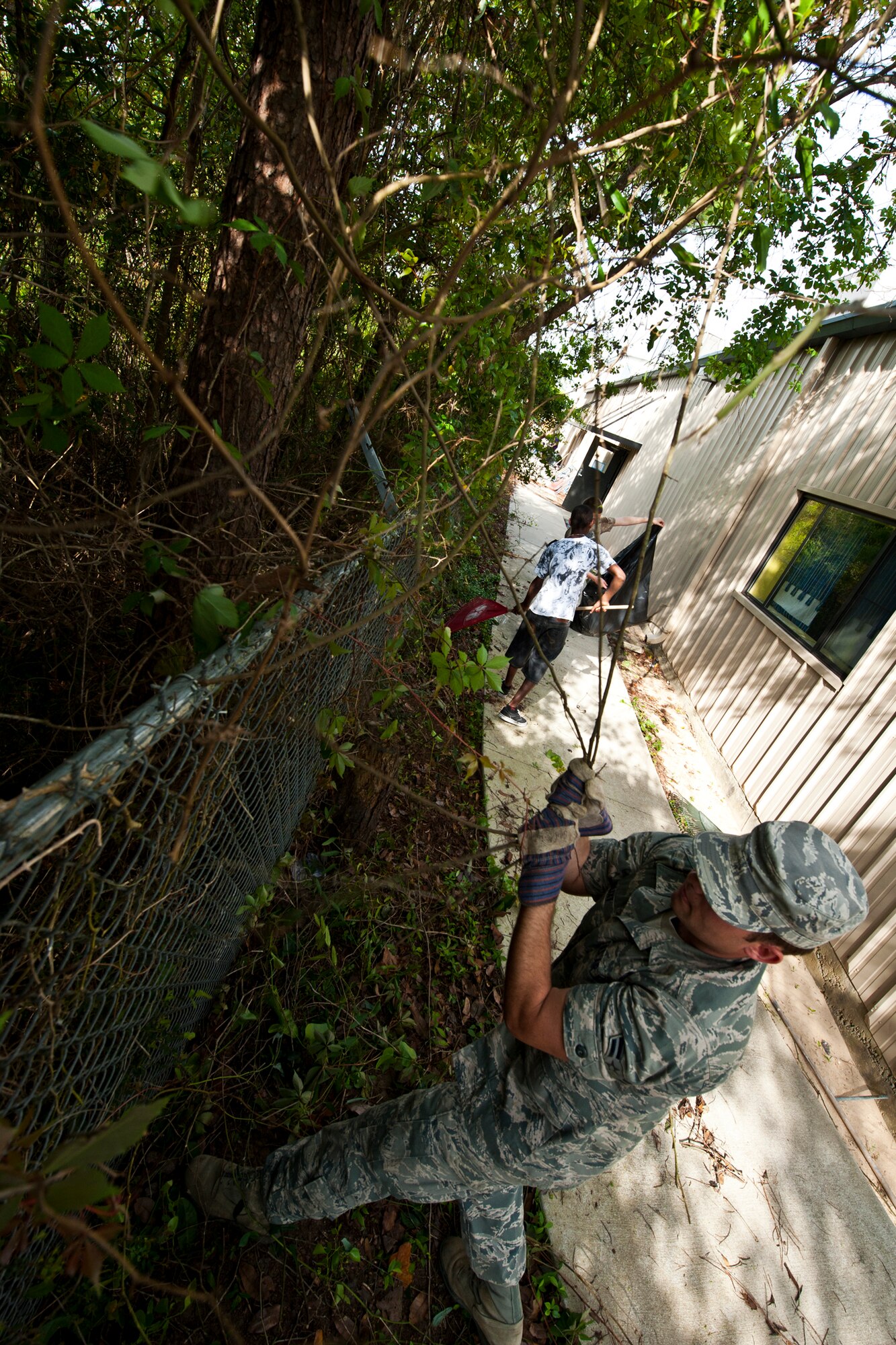 Airman 1st Class Shannon Blixt, a student at the Navy School of Explosive Ordnance Disposal, helps clear brush away from a fence at the Boys and Girls Club in Fort Walton Beach, Fla., March 21.  He and four other EOD students used their break from class to help clean up areas of the club.  (U.S. Air Force photo/Samuel King Jr.)