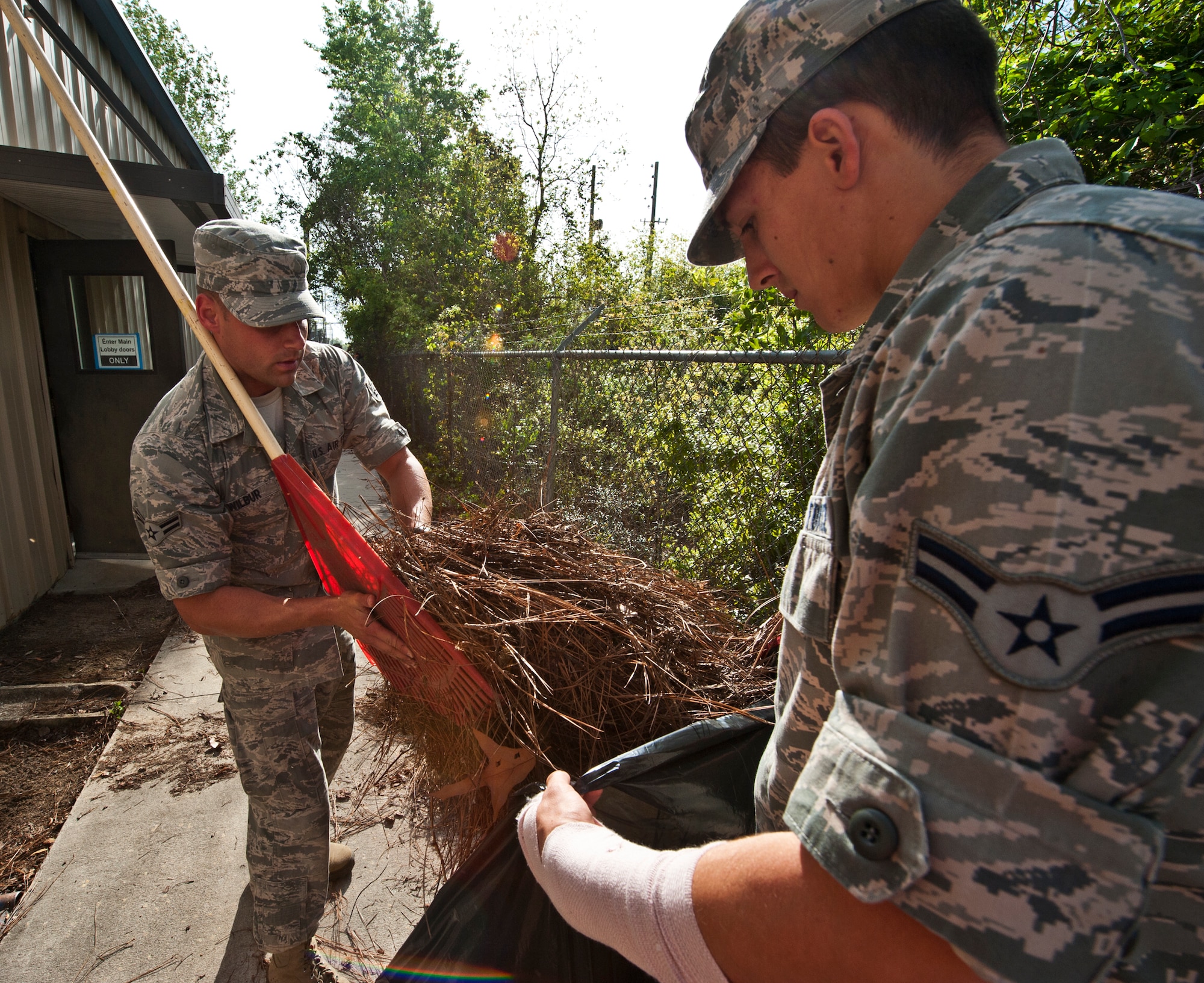 Airmen 1st Class Justin Wilbur and Christopher Smith pick up pine needles at the Boys and Girls Club in Fort Walton Beach, Fla., March 21.  During a break in their class schedule, the Airmen spent two hours cleaning and completing odd jobs for the local club.  (U.S. Air Force photo/Samuel King Jr.)