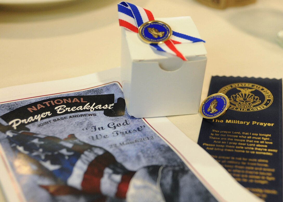 Tables display personal mementos such as a ribbon with the military prayer, a pendant and ceremonial program to set the theme for a National Prayer Breakfast at Joint Base Andrews, Md., on March 22. The theme of this year's ceremony was "In God We Trust." (U.S. Air Force photo/Staff Sgt. Nichelle Anderson)