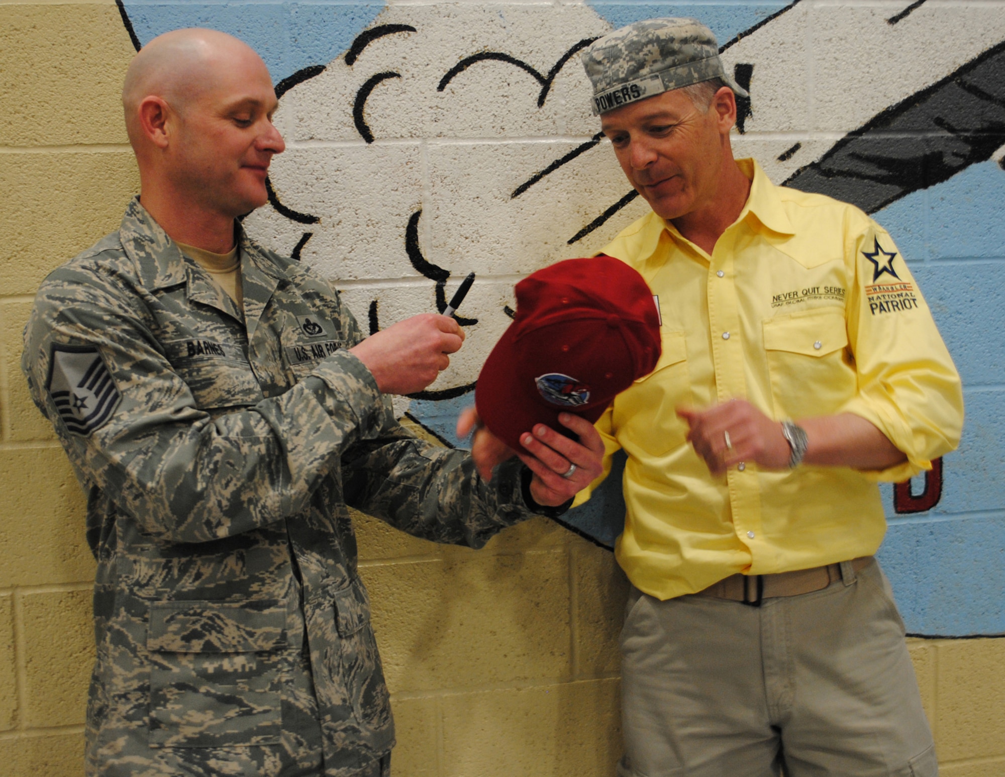 Master Sgt. Jeffery Barnes, 819th RED HORSE Squadron airfields, hands Powers an official "Dirt Boys" hat after signing it on behalf of the squadron.   (U.S. Air Force photo/Airman 1st Class Cortney Paxton)