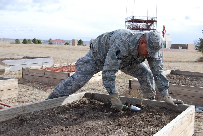 Staff Sgt. Mario Jaramillo, Air Force Space Command protocol office, cleans out one of the community garden beds at Peak View Park so fertilizer can be spread. The gardens are open to the Peterson Community to plant and harvest throughout the summer. (U.S. Air Force photo/Lea Johnson)