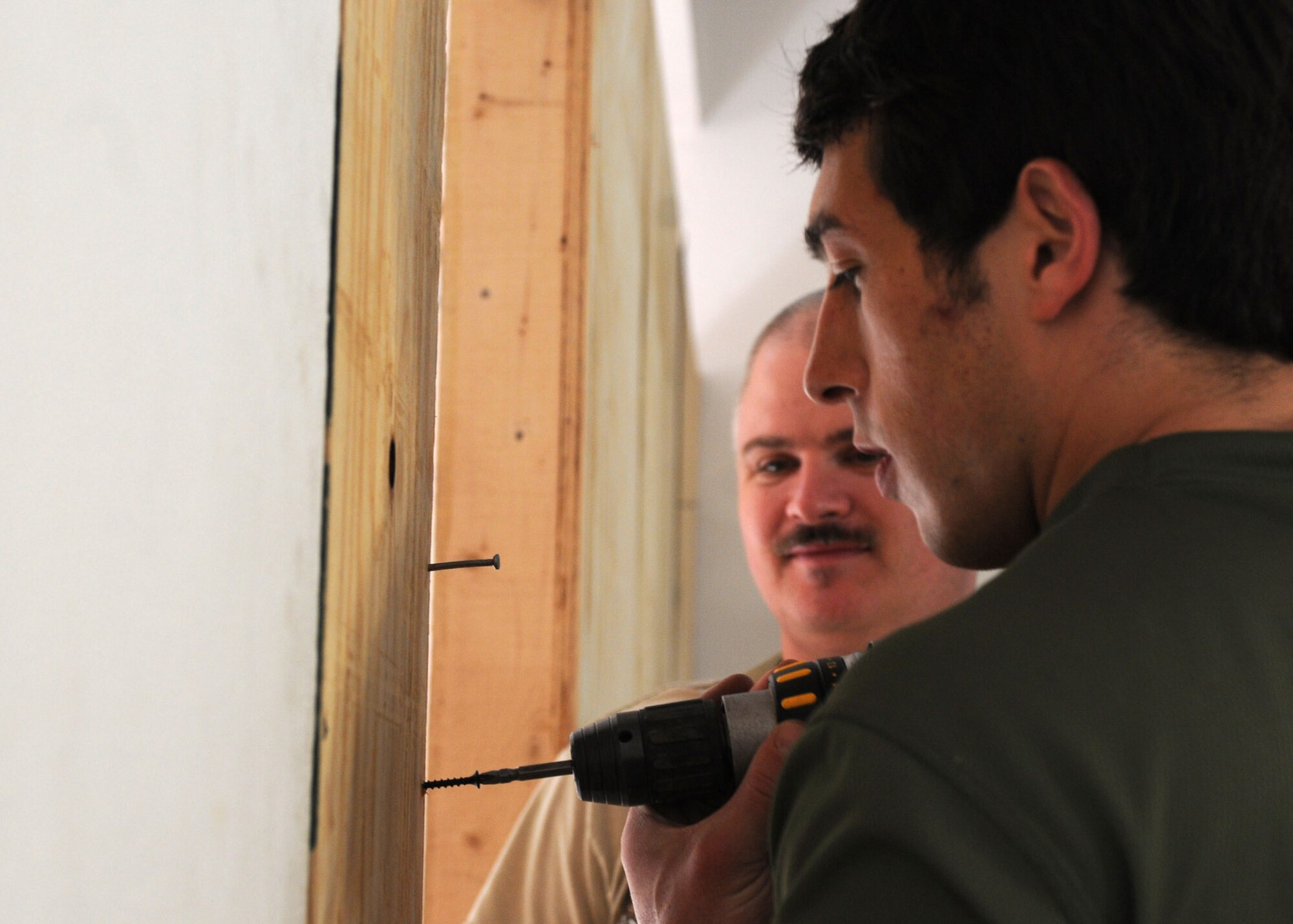 Royal Air Force Flight Lt. Tom Loucaides, 438th Air Expeditionary Wing Thunder Lab director of aviation training, and U.S. Navy Petty Officer 1st Class Robert Hay, 438th AEW Thunder Lab leadership and professionalism director, screw in the final wall sheets of wood during the building of a classroom at Shindand Air Base, Afghanistan, March 21, 2012. The advisers helped build classrooms, a multipurpose room and an aviation simulator room that will be used as Shindand’s English language training center (SELTC) for the Afghan air force Thunder Lab pilot candidates. (U.S. Air Force photo by Staff Sgt. Nadine Y. Barclay)