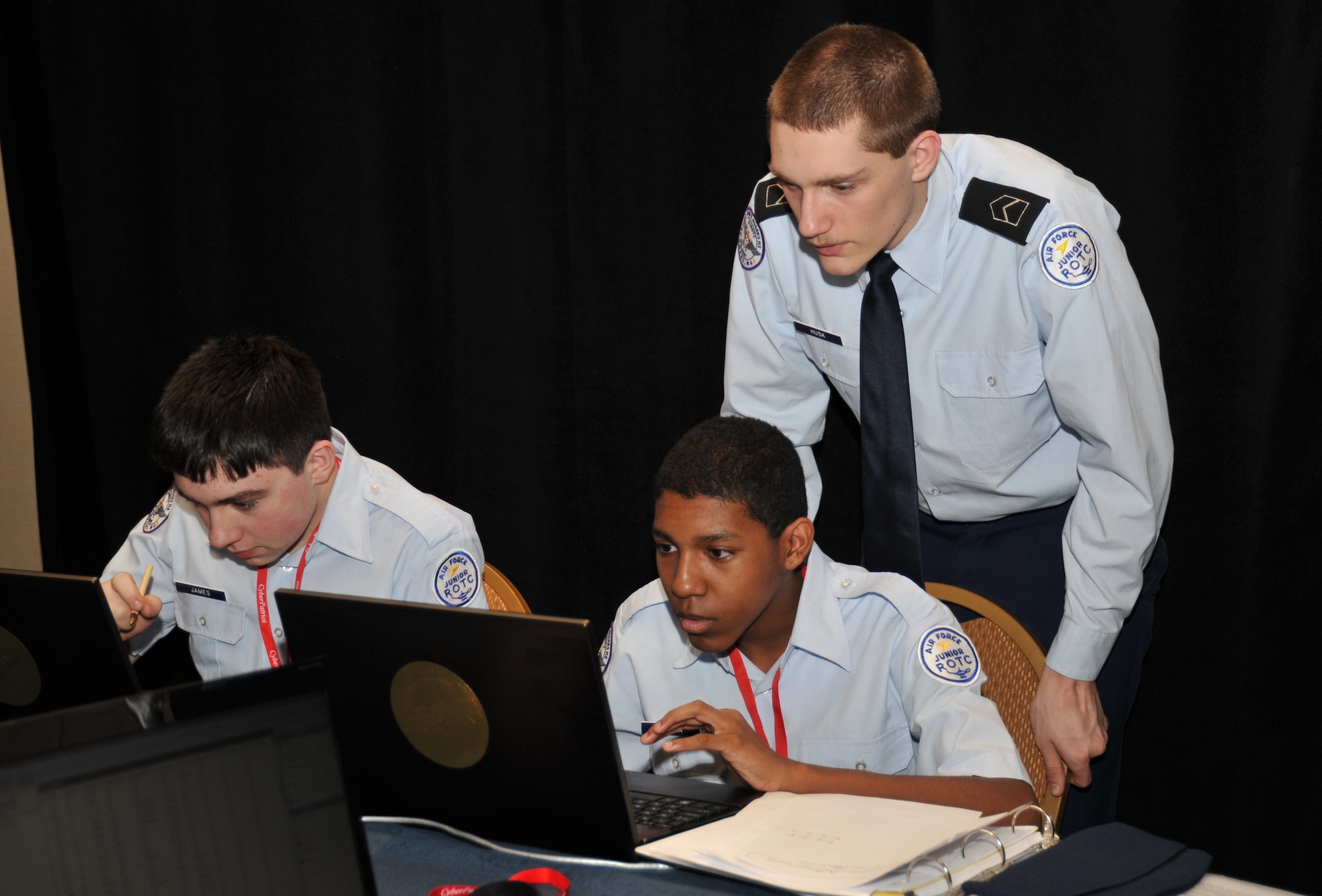 Air Force Junior ROTC Cadet 2nd Lt. Clayton Husk, at back, assists Cadet Airman Chamberlain James, left, and Cadet Airman Joseph Ceniza in closing loopholes in their network security during the CyberPatriot IV competition at the National Harbor, Md., March 23, 2012. Their team, ‘Air Pirates’, from Spokane, Wash., went on to win second place in the All-Service Division of the event. (U.S. Air Force photo/Airman 1st Class Alexander W. Riedel)