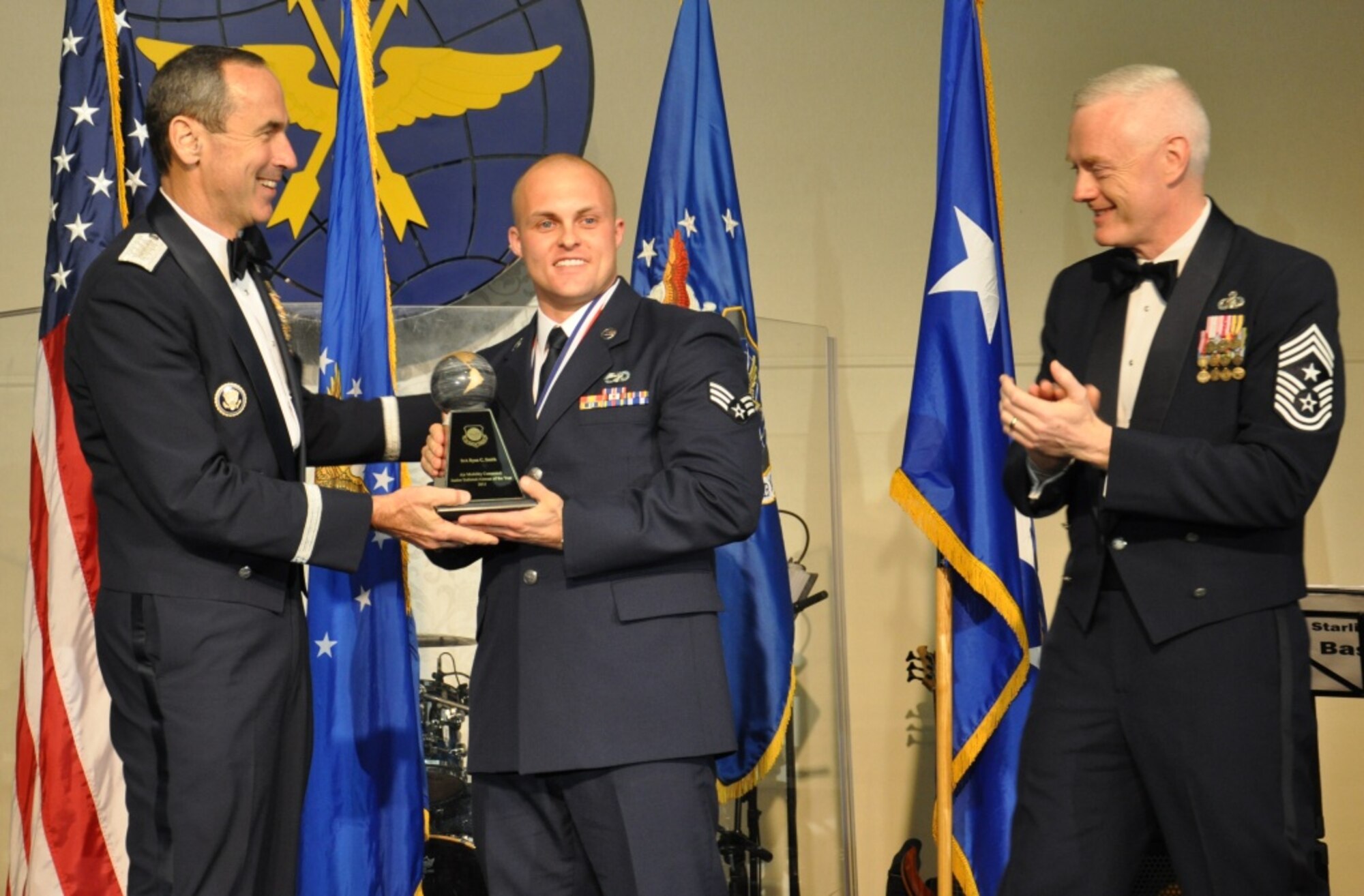 JOINT BASE McGUIRE-DIX-LAKESURST, N.J. -- Gen. Ray Johns, Air Mobility Command commander, and Command Chief Master Sgt. Richard Kaiser, AMC command chief, present the award for Airman of the Year to Senior Airman Ryan Smith, 3rd Aerial Port Squadron, Pope Field, N.C., during the AMC Outstanding Airman of the Year banquet that took place at Scott AFB, Ill., March 21. Smith is a passenger service agent who helped move more than 200,000 passengers on more than 10,000 missions in support of both in-garrison and overseas contingency operations. (U.S. Air Force photo by 1st Lt. Sybil Taunton, U.S. Air Force Expeditionary Center Public Affairs)