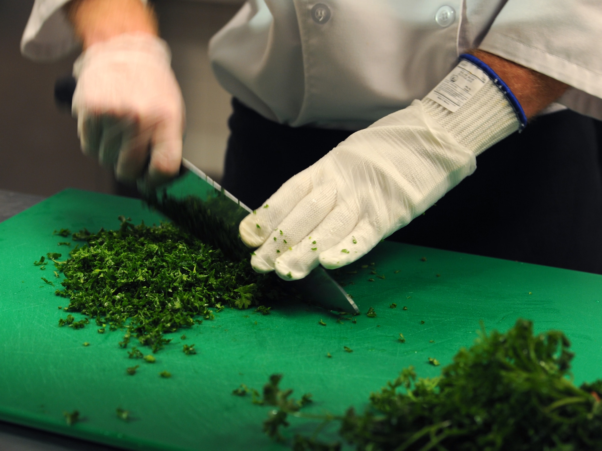 Senior Airman Brady McDede, 6th Force Support Squadron food service technician, chops parsley to be used in Manhattan clam chowder, at the Citi Bank corporate building in Tampa, Fla., March 23, 2012. McDede was sent by 6th FSS to train with civilan chefs to help improve the dining conditions on MacDill Air Force Base, Fla. (U.S. Air Force photo by Airman Basic David Tracy)