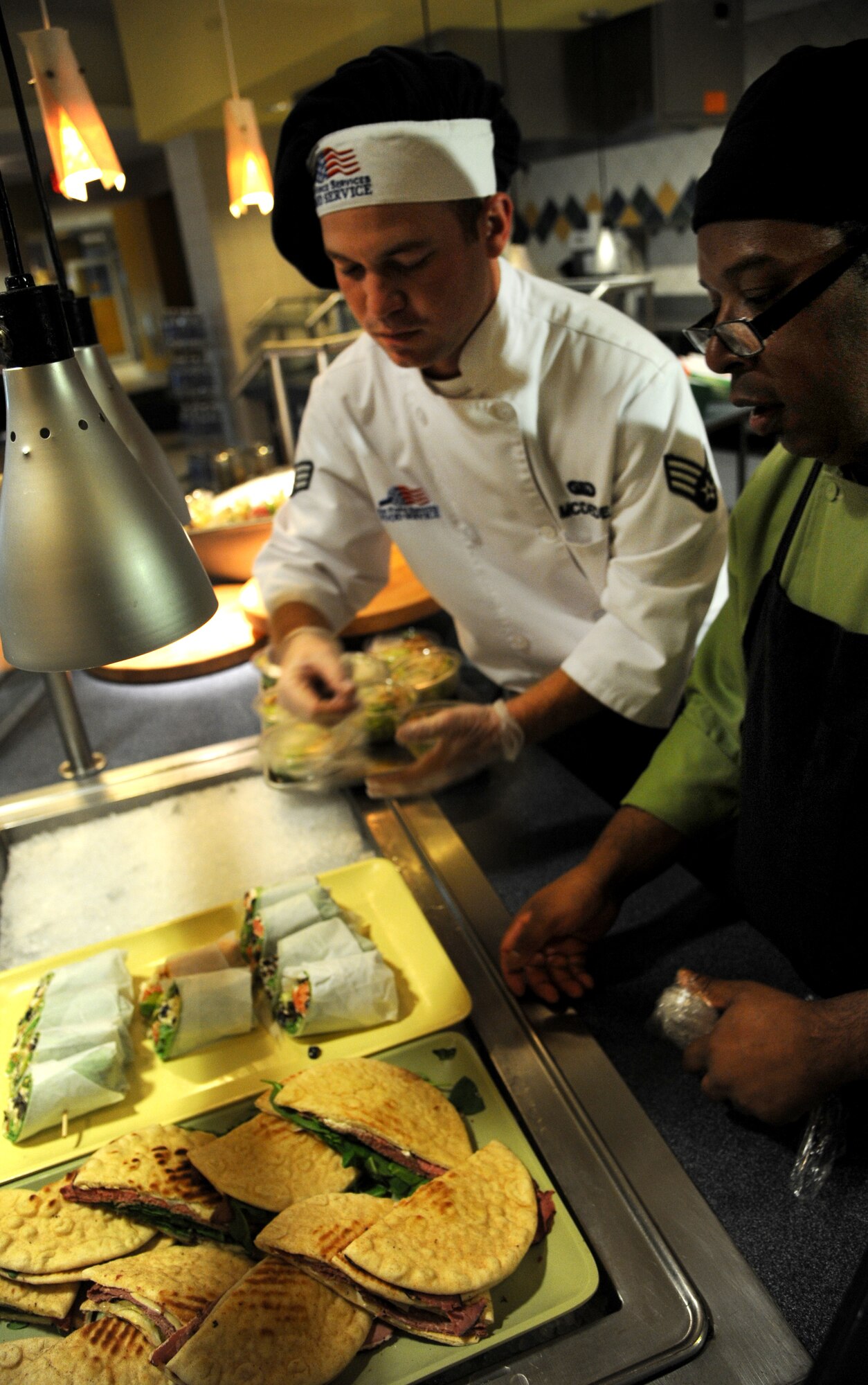 Francisco Mercedes, a line cook, instructs Senior Airman Brady McDede, 6th Force Support Squadron food service technician, on how to lay out sandwiches for display at the Citi Bank corporate building in Tampa, Fla., March 23, 2012. McDede has been training with civilian chefs to help improve the dining conditions on MacDill Air Force Base, Fla. (U.S. Air Force photo by Airman Basic David Tracy)