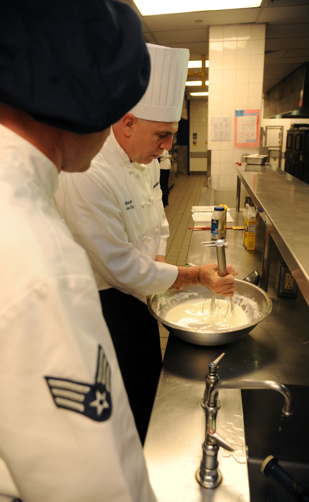 Senior Airman Brady McDede, 6th Force Support Squadron food service technician, observes stirring techniques performed by Executive Chef, John Hackett, at the Citi Bank corporate building in Tampa, Fla., March 23, 2012. McDede was sent by 6th FSS to train with civilan chefs to help improve the dining conditions on MacDill Air Force Base, Fla. (U.S. Air Force photo by Airman Basic David Tracy)