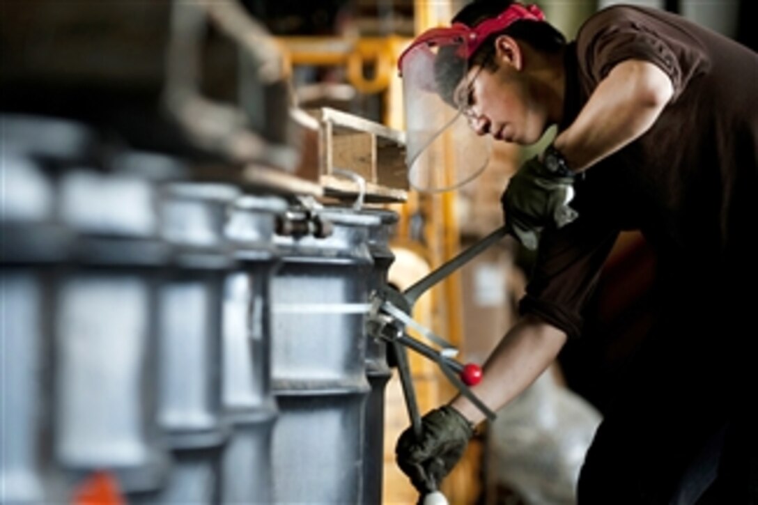 U.S. Navy Seaman Erickson Schafer bands barrels of hazardous waste for offload to a Military Sealift Command ship aboard the aircraft carrier USS Carl Vinson in the Arabian Sea on March 15, 2012.  Schafer is an aviation structural mechanic airman assigned to the Supply Department's S-8 Division.  